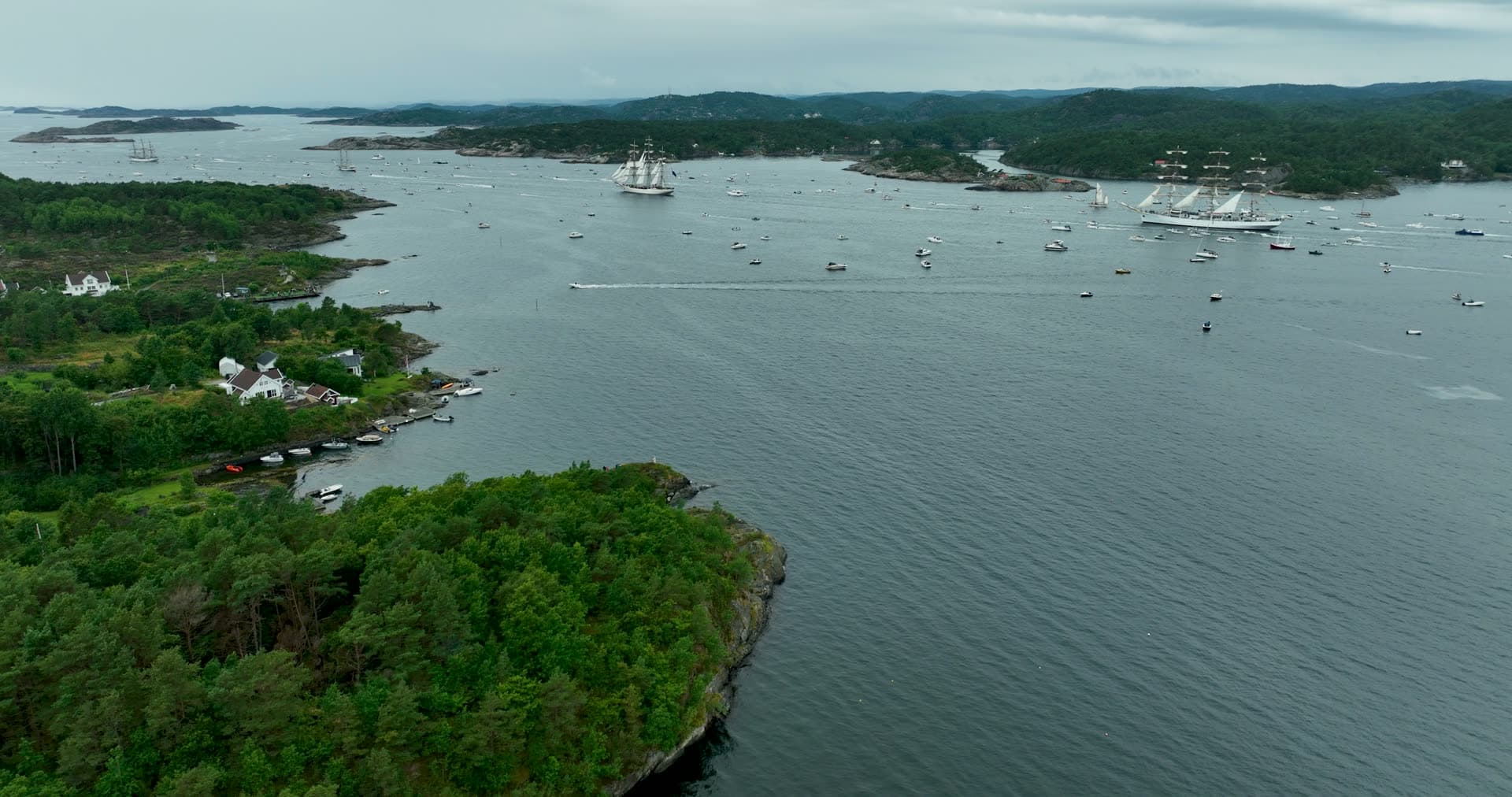 Tall ships and boat fleet off wooded point, Kristiansand, Norway