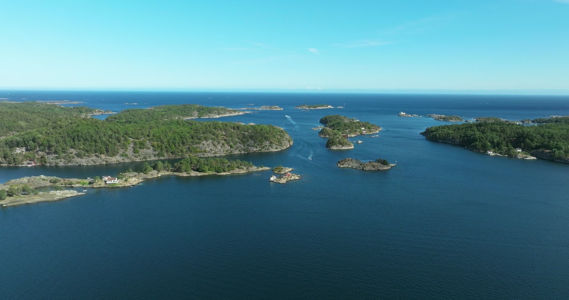 Boat wake in strait between wooded islets, Lillesand, Norway