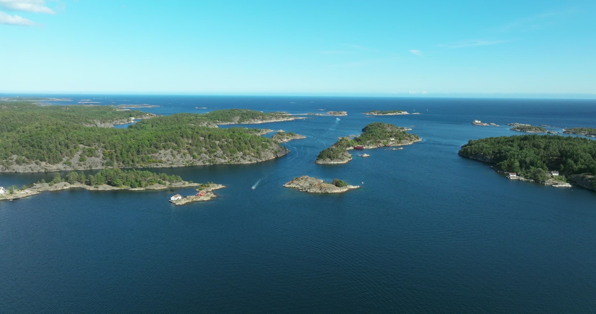 Small boat passing red cabins in the skerries, Lillesand, Norway