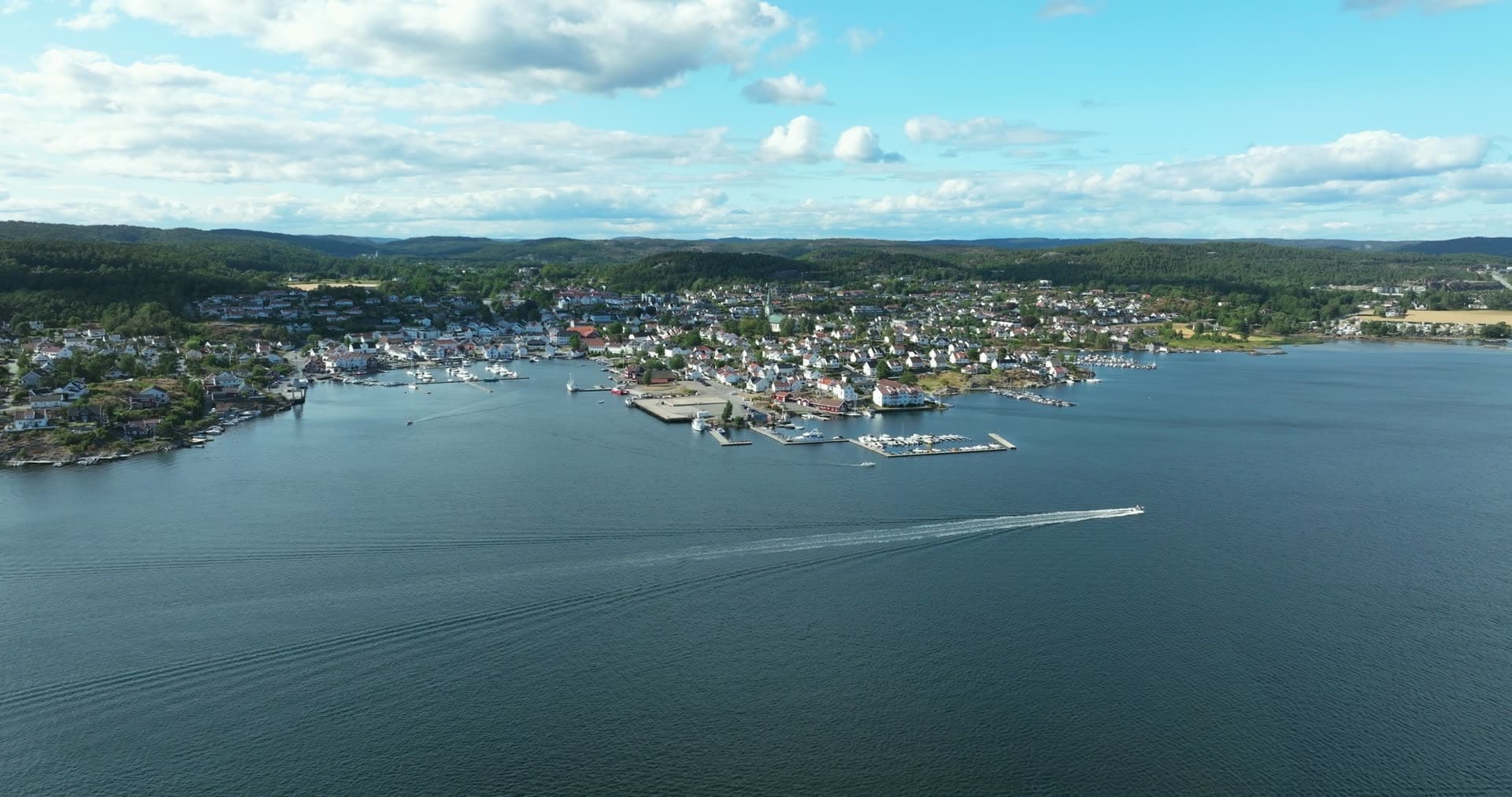 Speedboat wake off marina piers and white houses, Lillesand, Norway