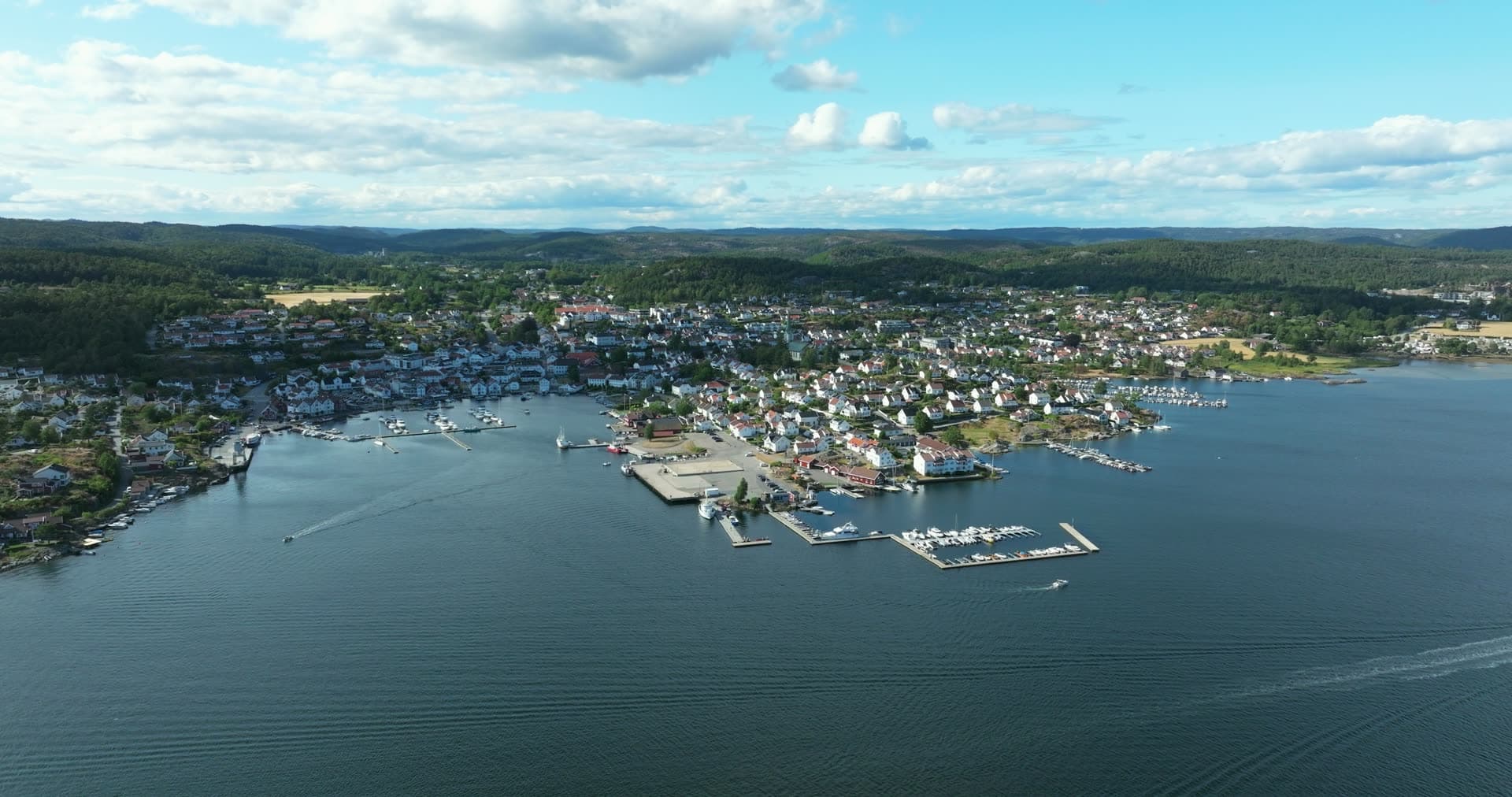 Marina piers and boat wake off white town, Lillesand, Norway