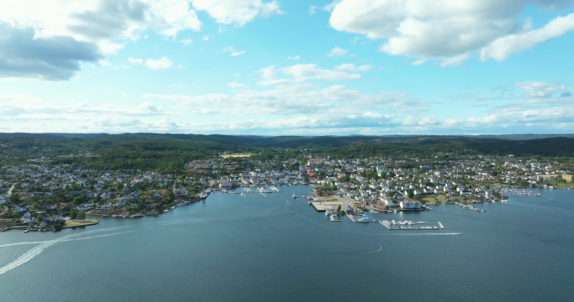 Speedboat wake off marina piers and white town, Lillesand, Norway