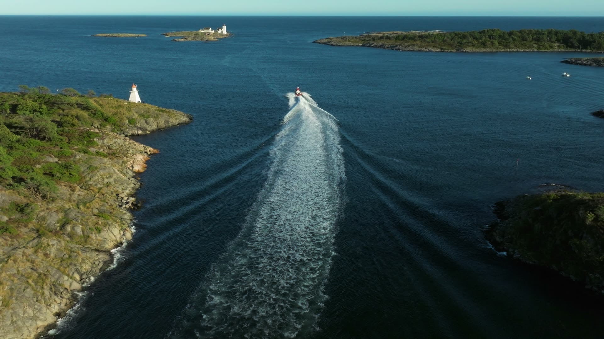 Red boat wake past white beacon and islets, Lillesand, Norway