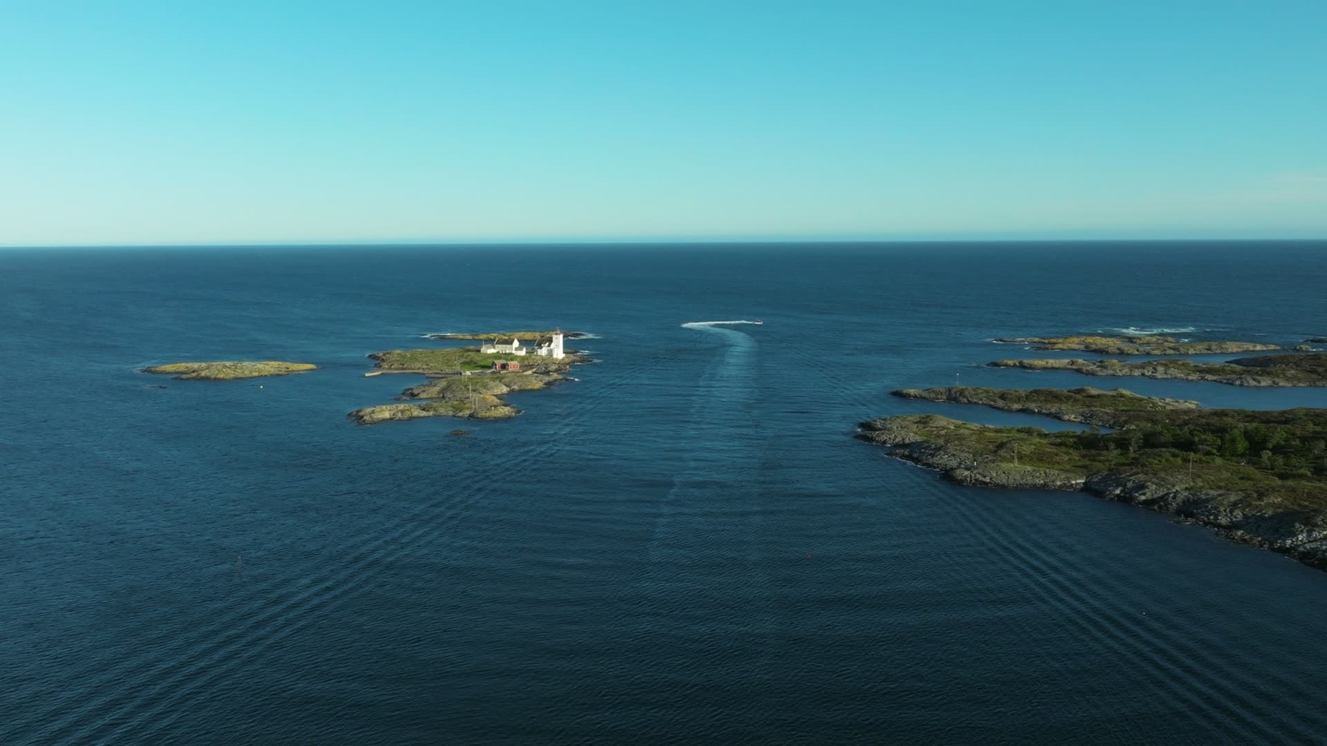 Boat wake past lighthouse islet to open sea, Lillesand, Norway