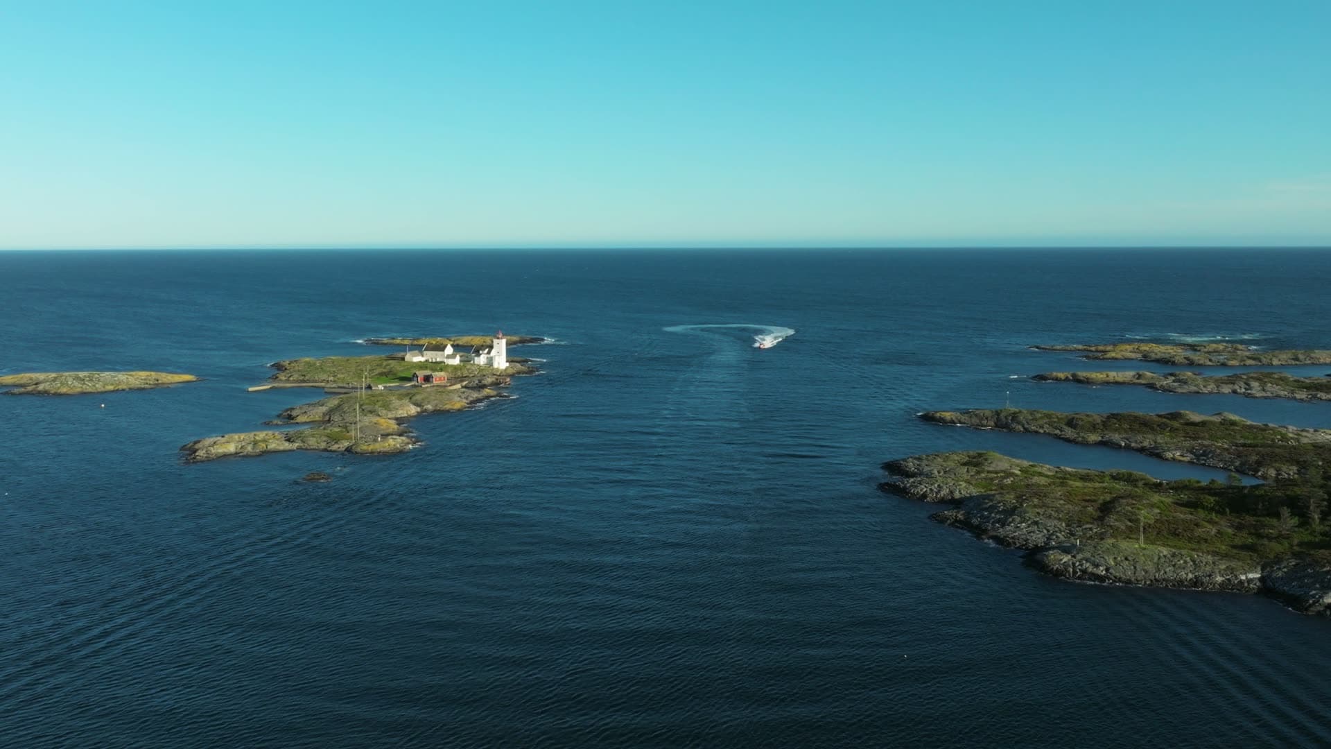 Boat wake past lighthouse islet at sea, Lillesand, Norway