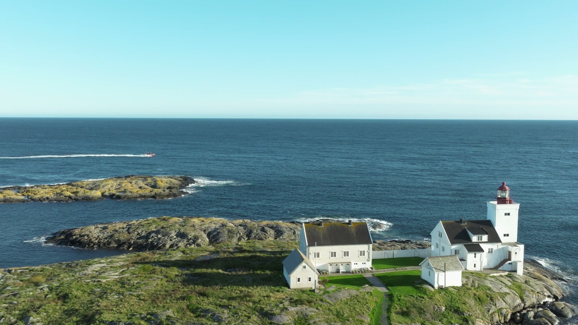 Speedboat passing lighthouse on rocky point, Lillesand, Norway