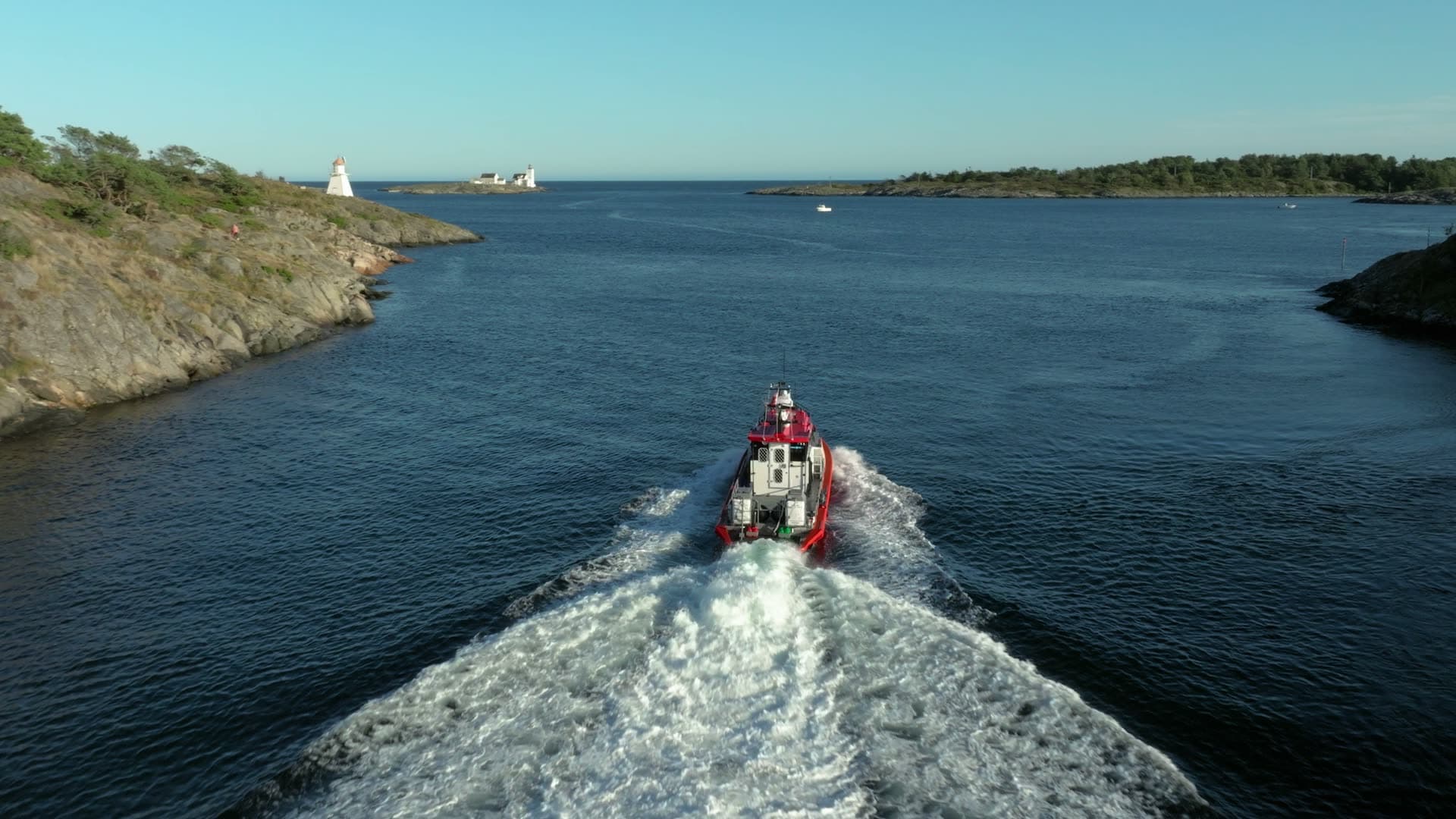 Red pilot boat wake past small lighthouse, Lillesand, Norway