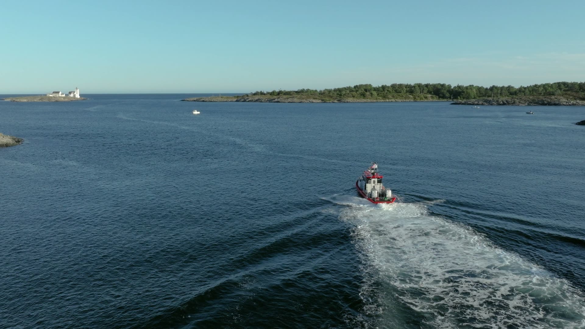 Red workboat trailing wake past lighthouse, Lillesand, Norway