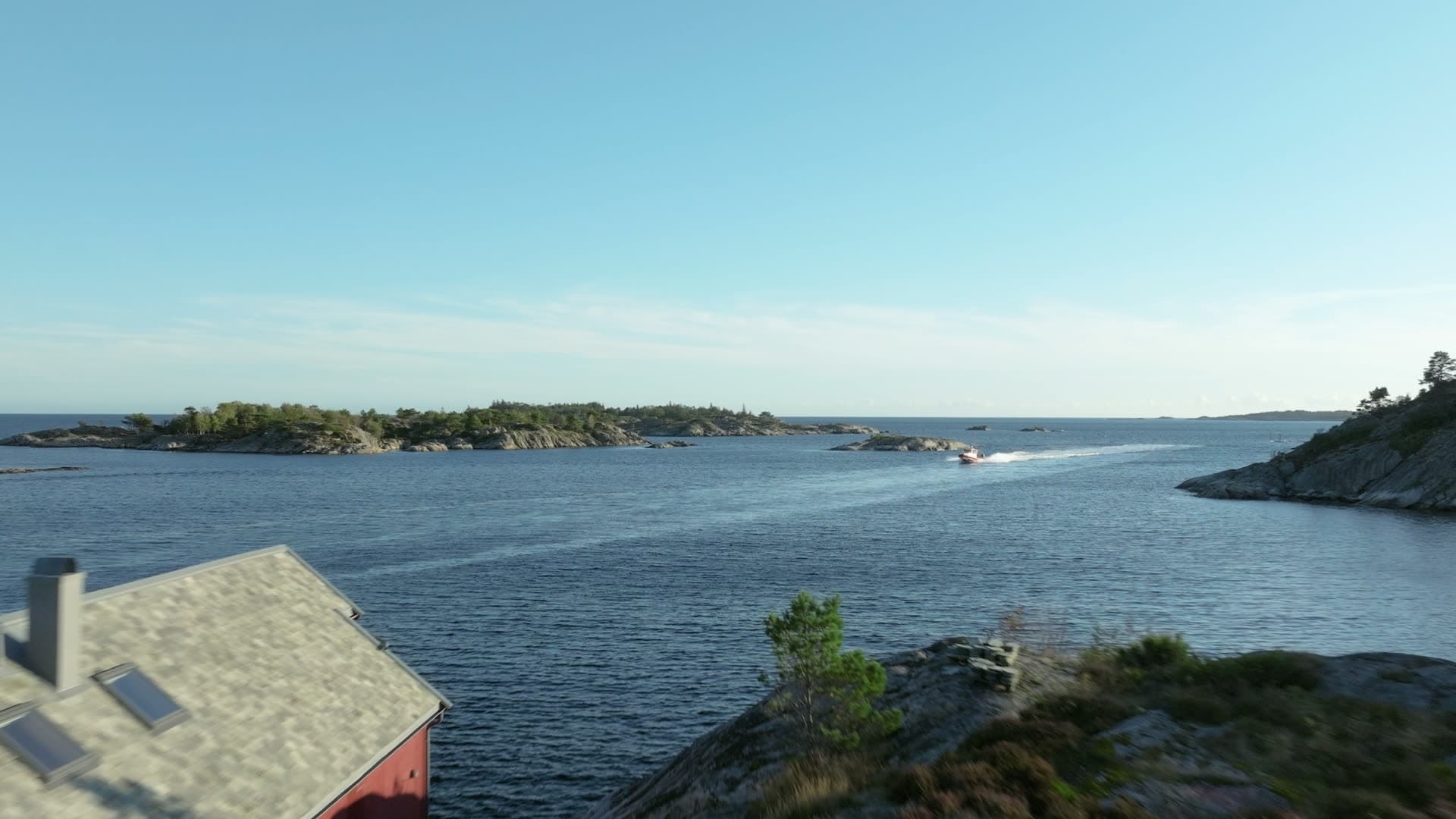 Red rescue boat speeding past red boathouse, Lillesand, Norway