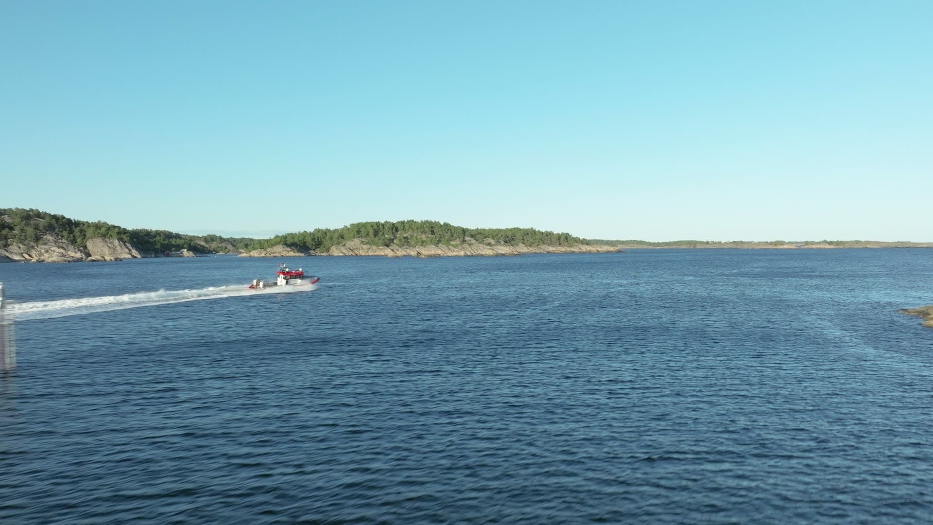 Red speedboat trailing wake past islets, Lillesand, Norway