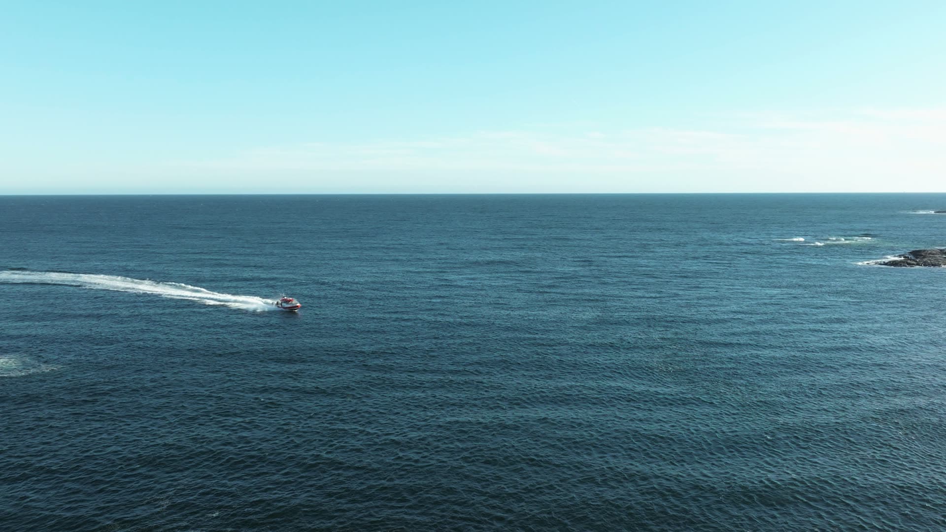 Fishing boat trailing wake past low skerries, Lillesand, Norway