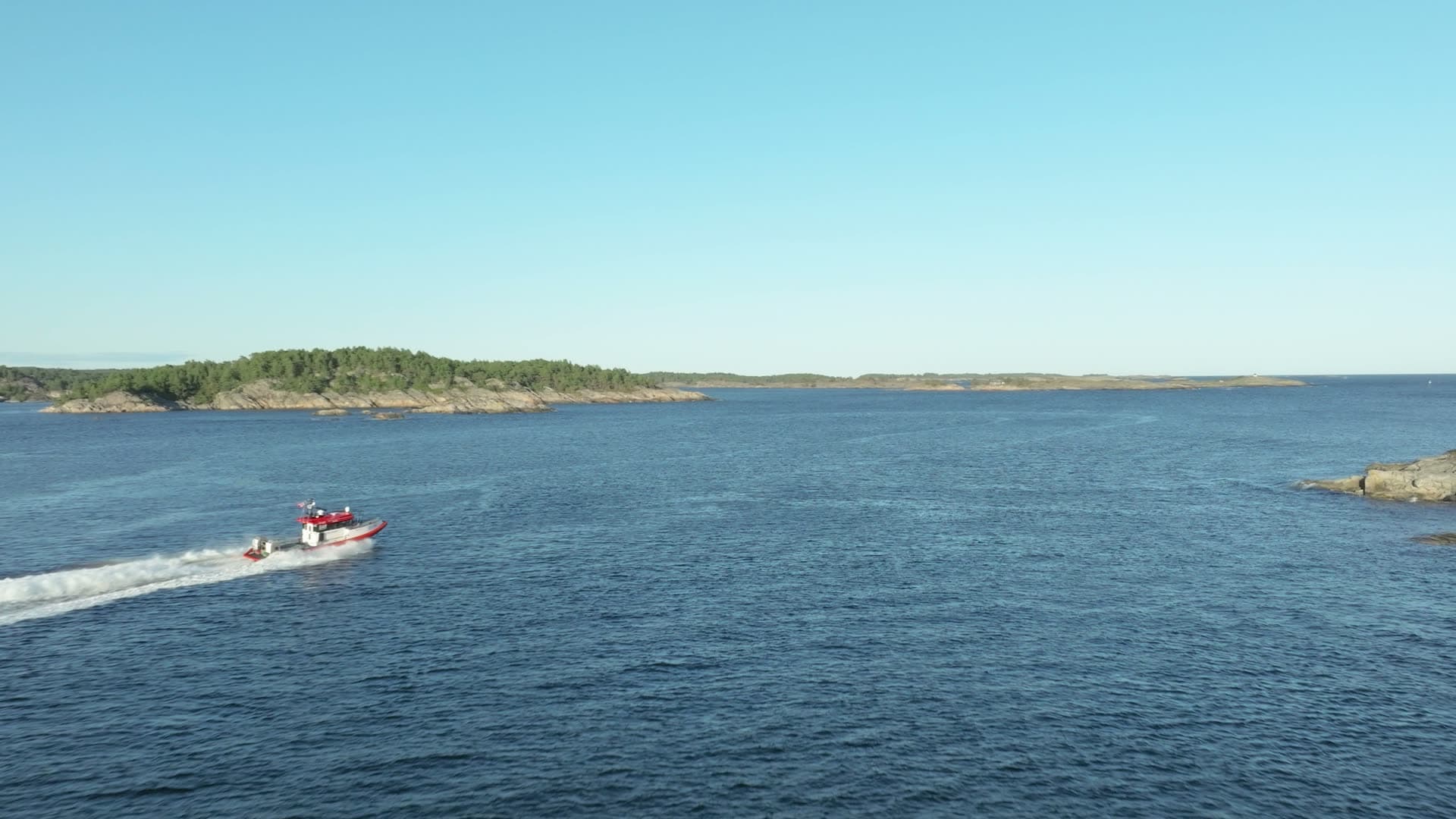 Red rescue boat wake past wooded islets, Lillesand, Norway