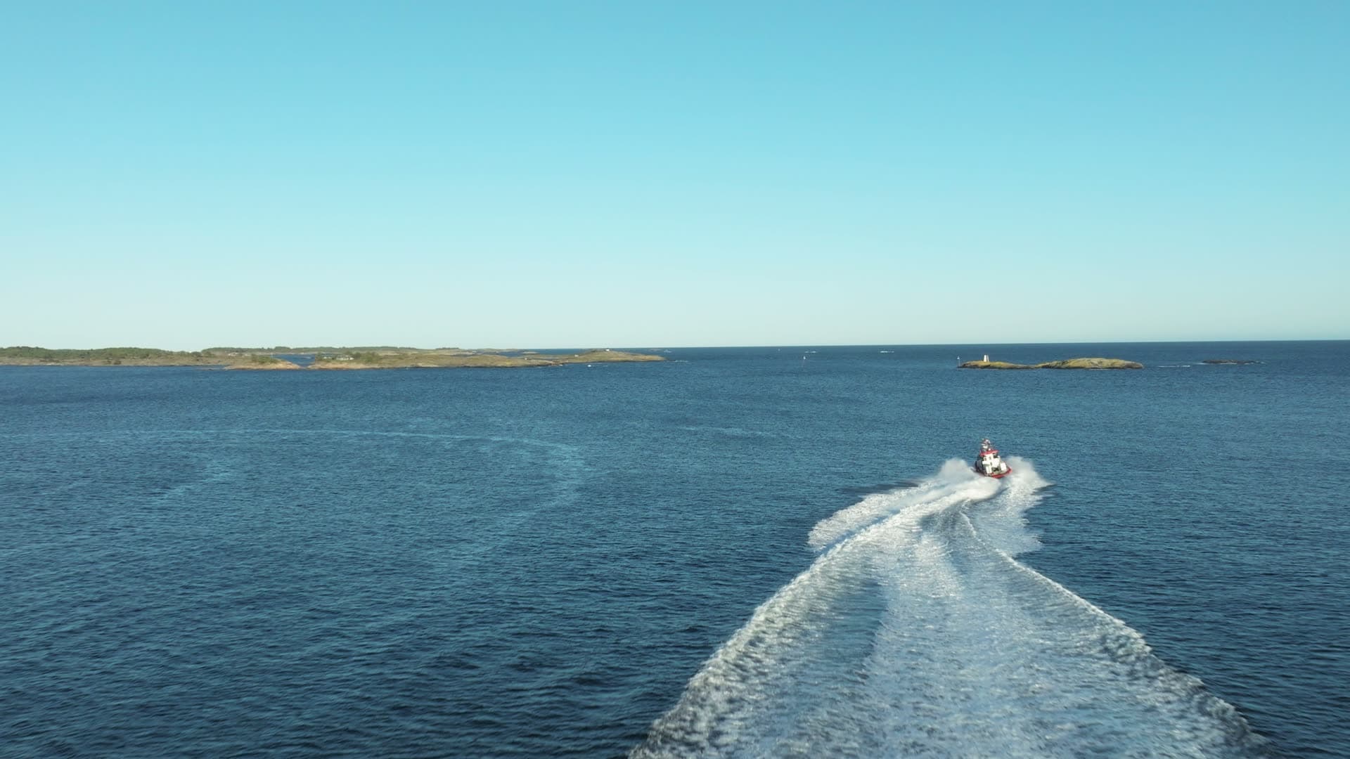 Red RIB carving wake past low skerries, Lillesand, Norway