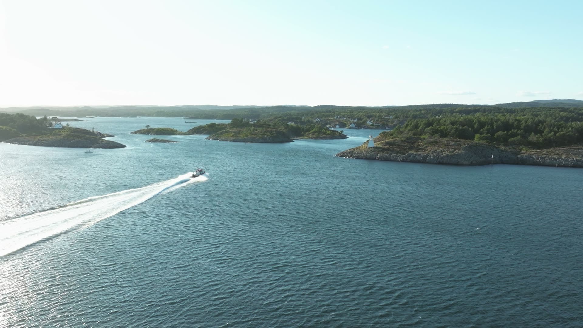 Speedboat wake past rocky islets and beacon, Lillesand, Norway