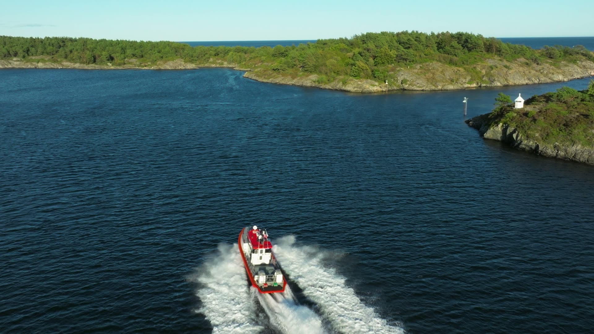 Red pilot boat speeding past beacon islet, Lillesand, Norway