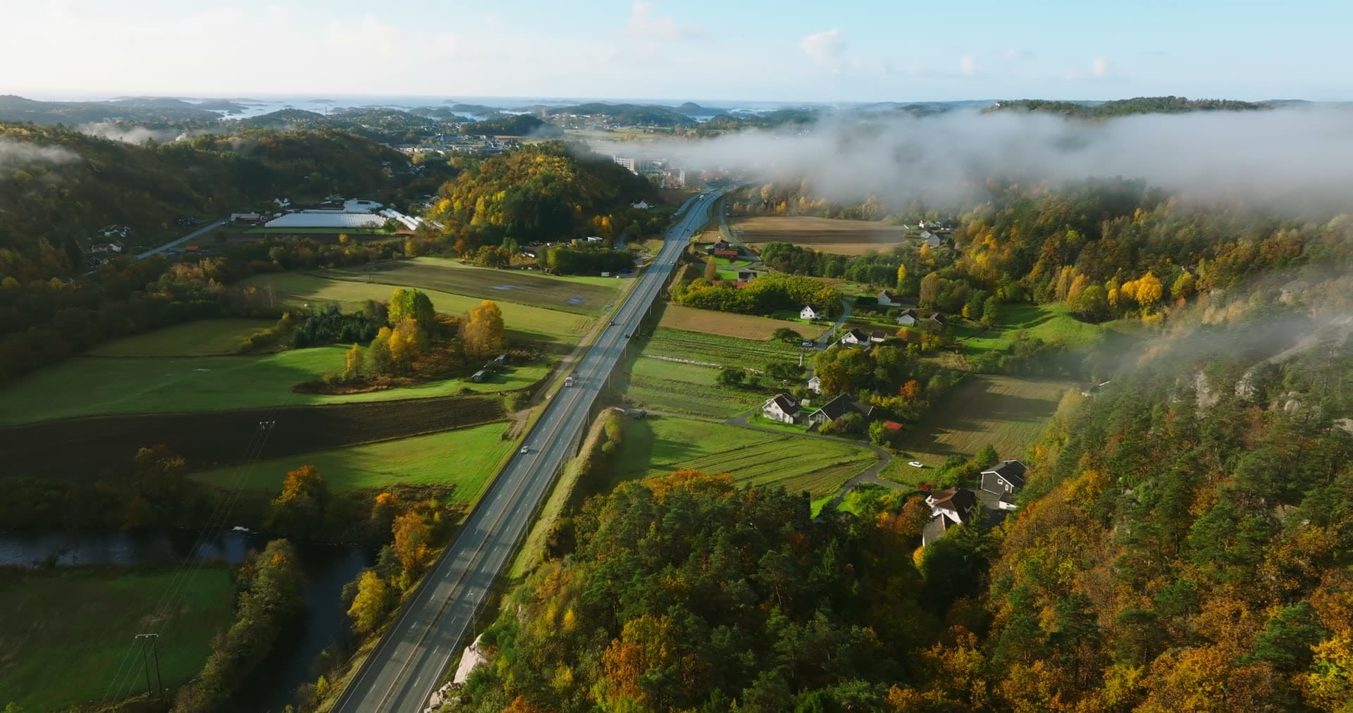 Highway through autumn farmland under fog, Monan, Norway