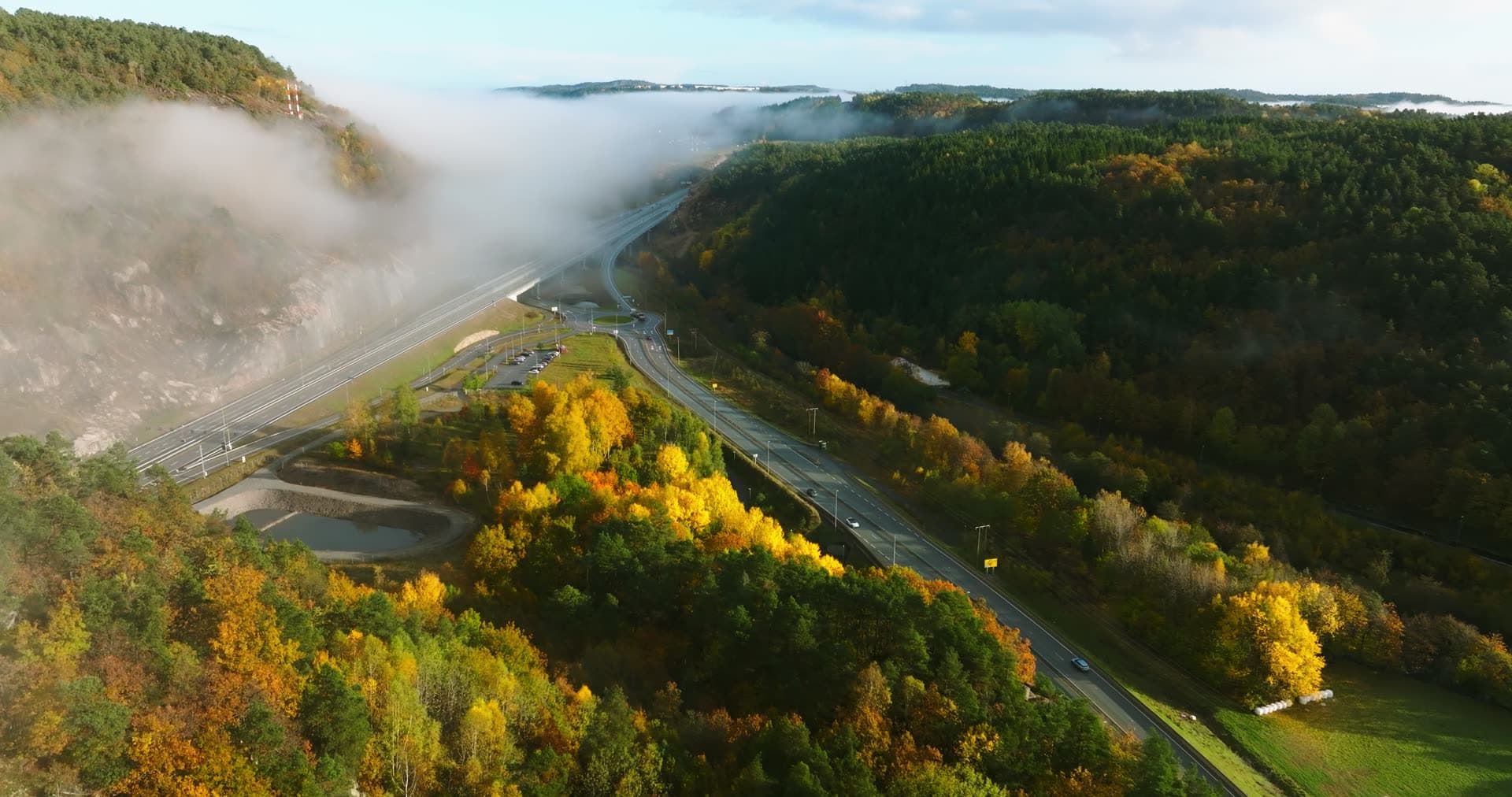 Fog drifting over highway cut in autumn valley, Monan, Norway