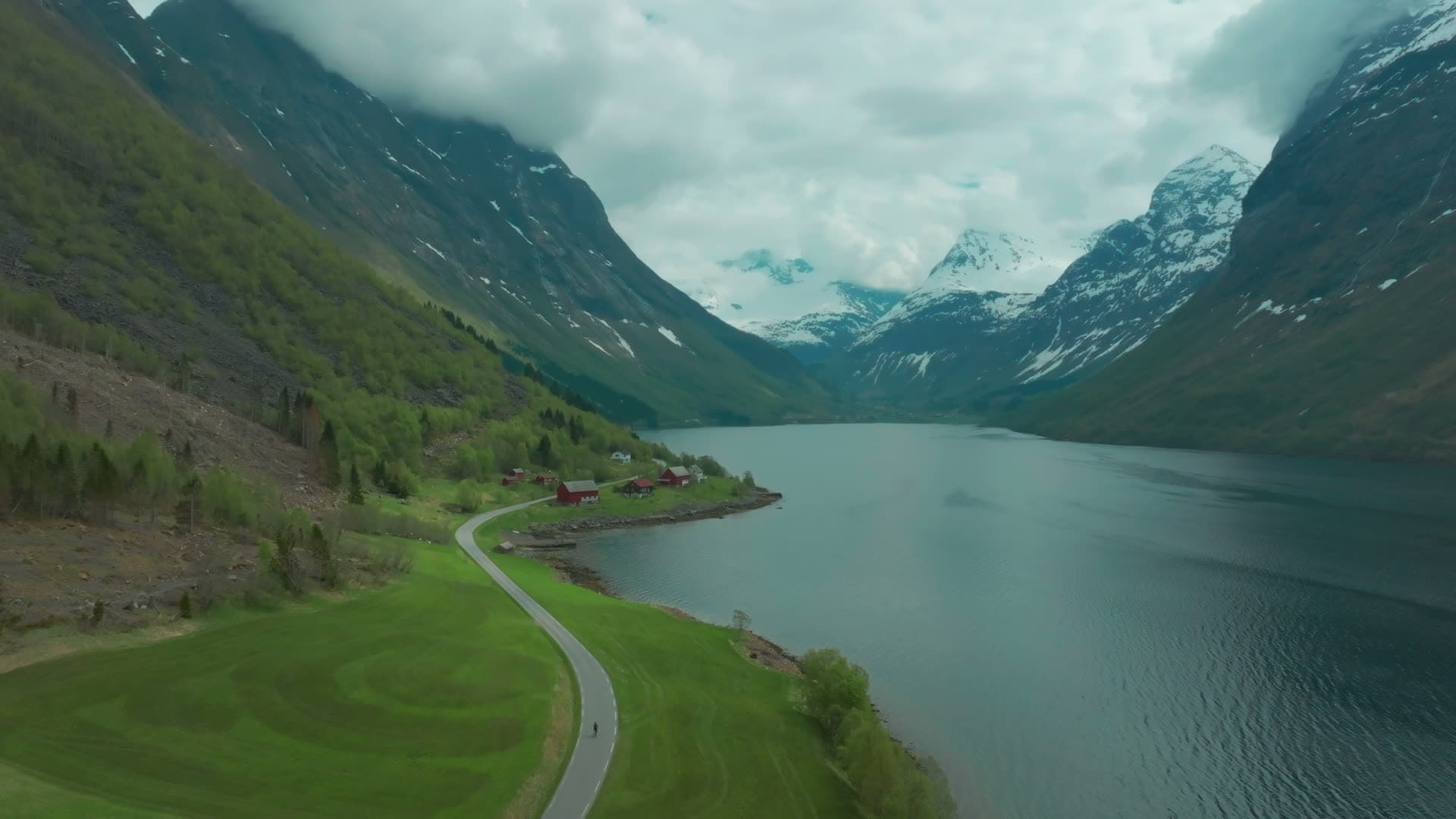 Lakeside road past red farms below snowy peaks, Norangsdalen, Norway