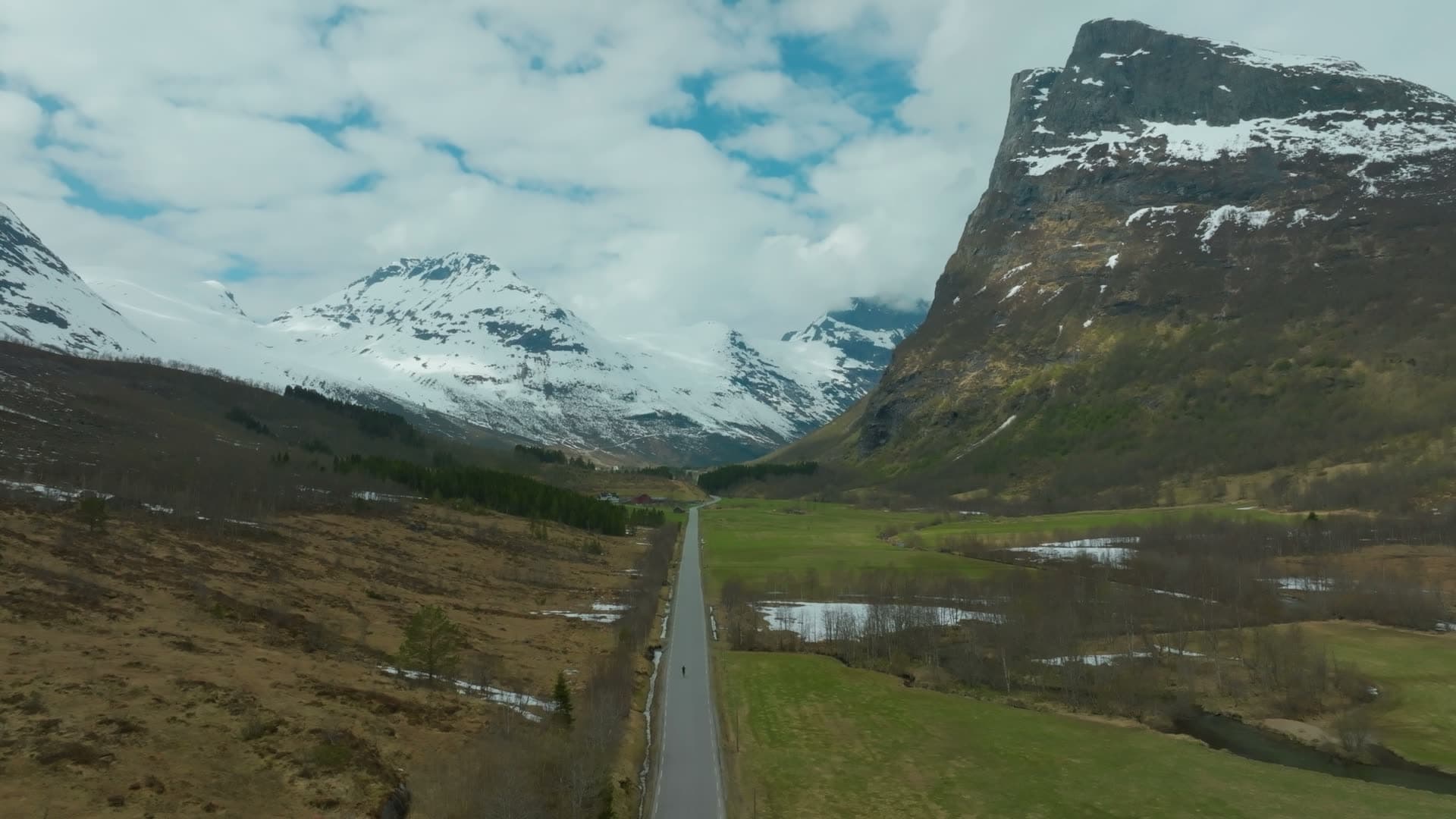 Cyclist on valley road below snowy peaks, Norangsdalen, Norway