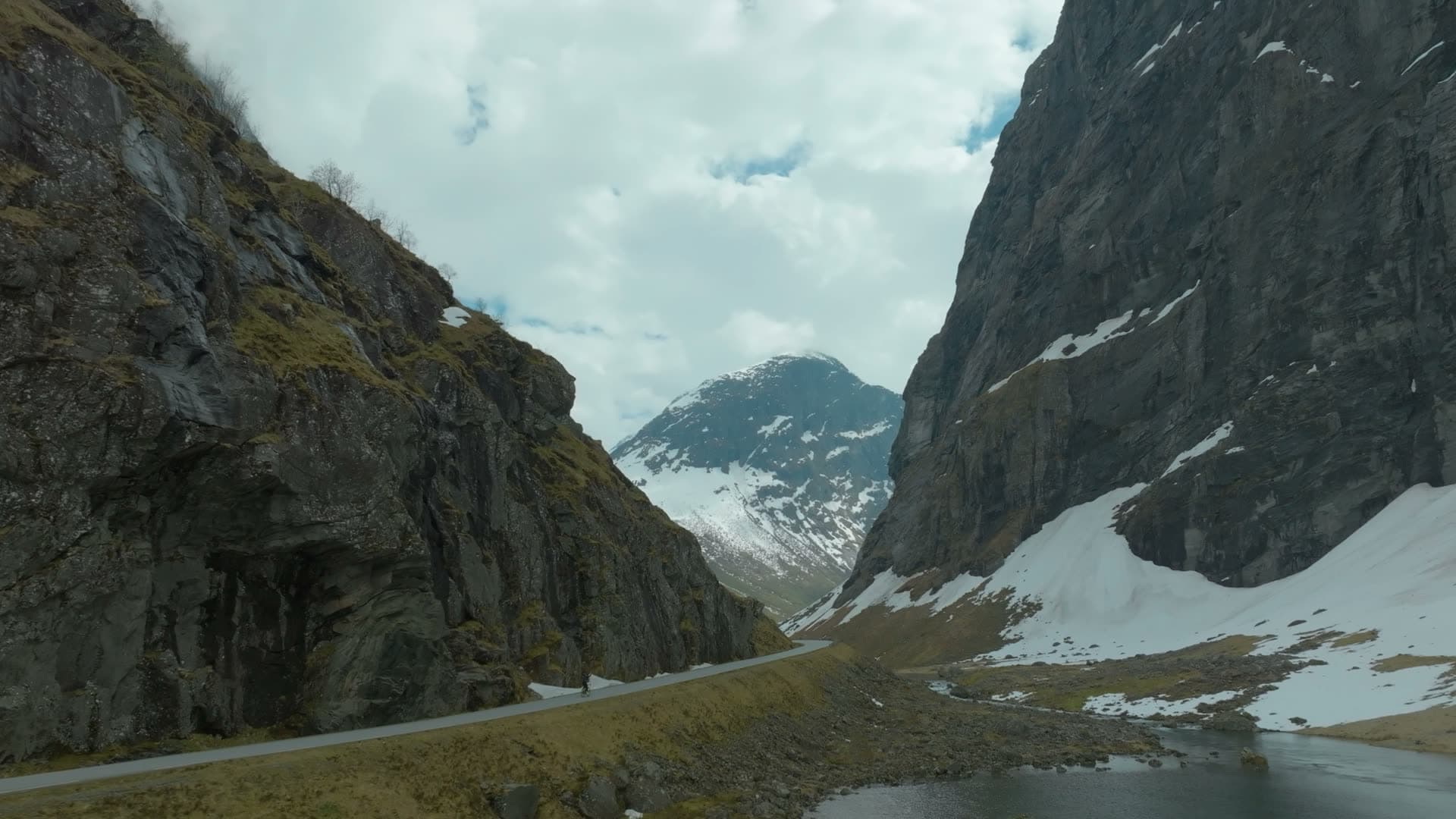 Road through narrow cliff valley, snow patches, Norangsdalen, Norway