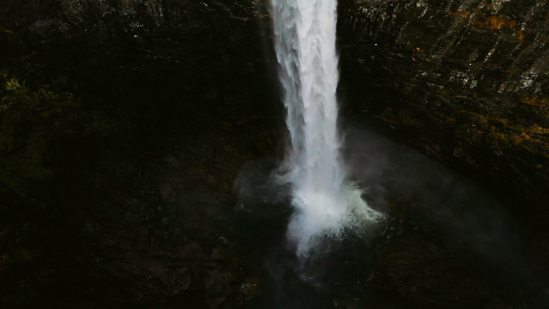 Waterfall plunging into dark rock plunge pool, Månafossen, Norway