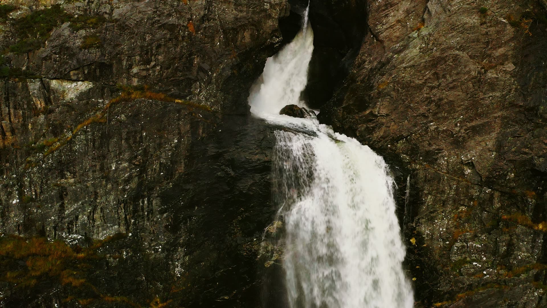 Waterfall splitting over dark rock ledge, Månafossen, Norway