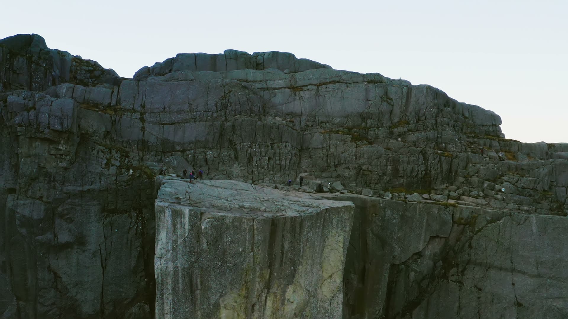 Hikers on shaded cliff plateau at dawn, Preikestolen, Norway