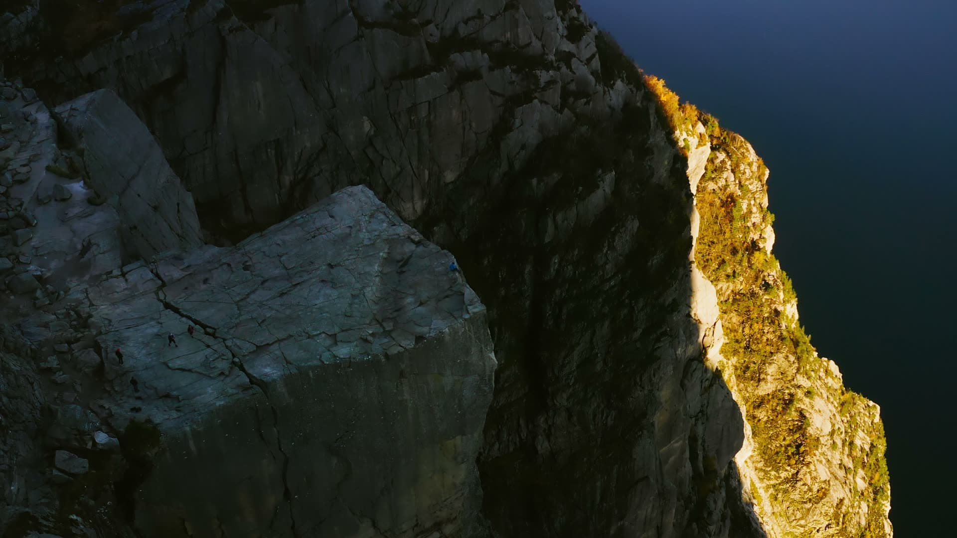 Sunlit cliff edge above dark fjord water, Preikestolen, Norway