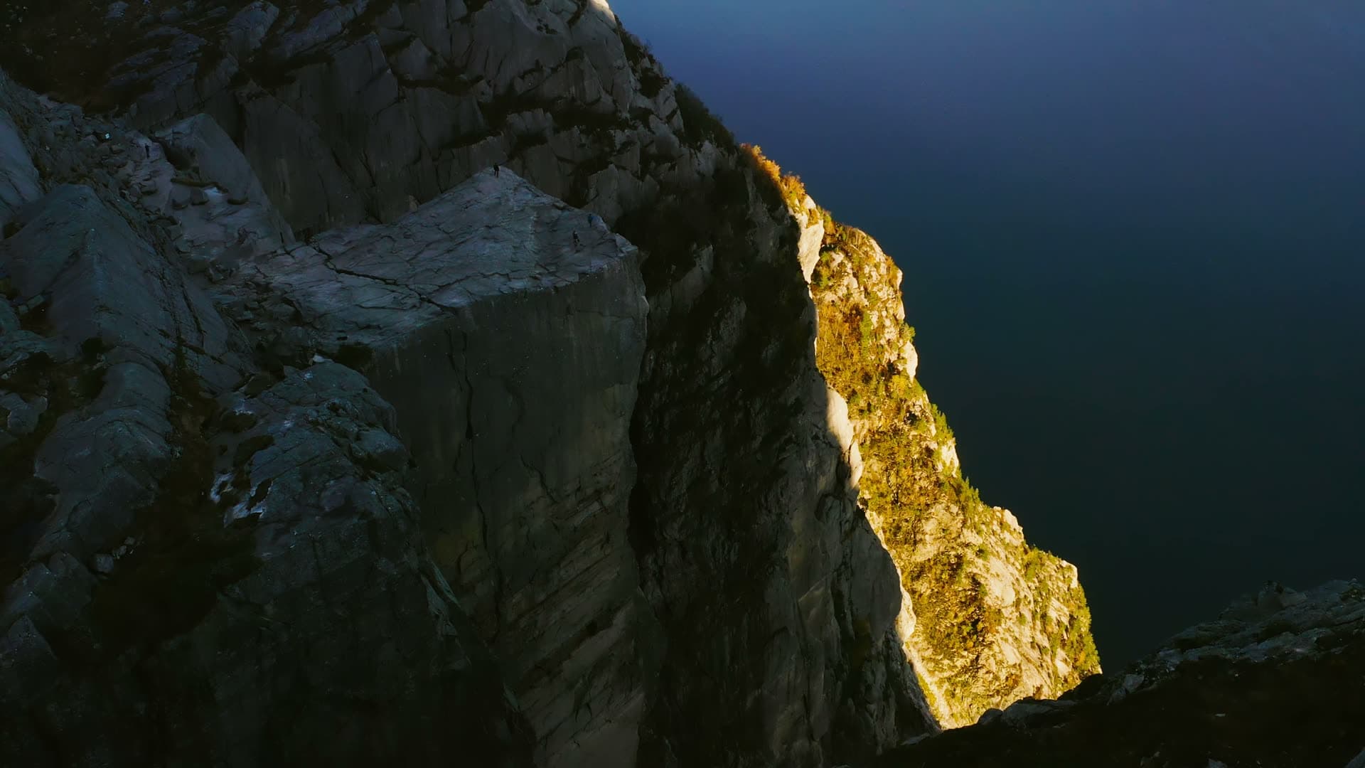 Sunlit cliff edge above dark fjord water, Preikestolen, Norway