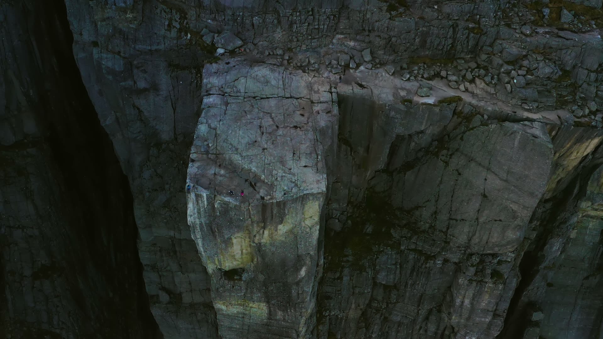 Few hikers on shadowed cliff plateau edge, Preikestolen, Norway
