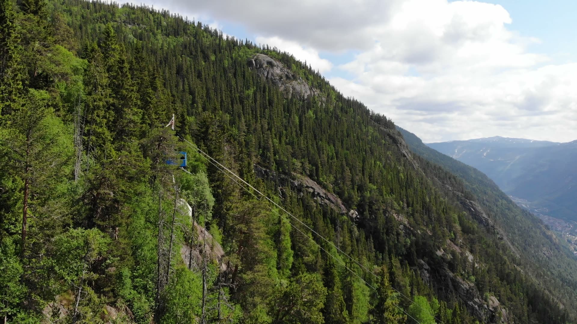 Blue cable car climbing forested cliff, Rjukan, Norway
