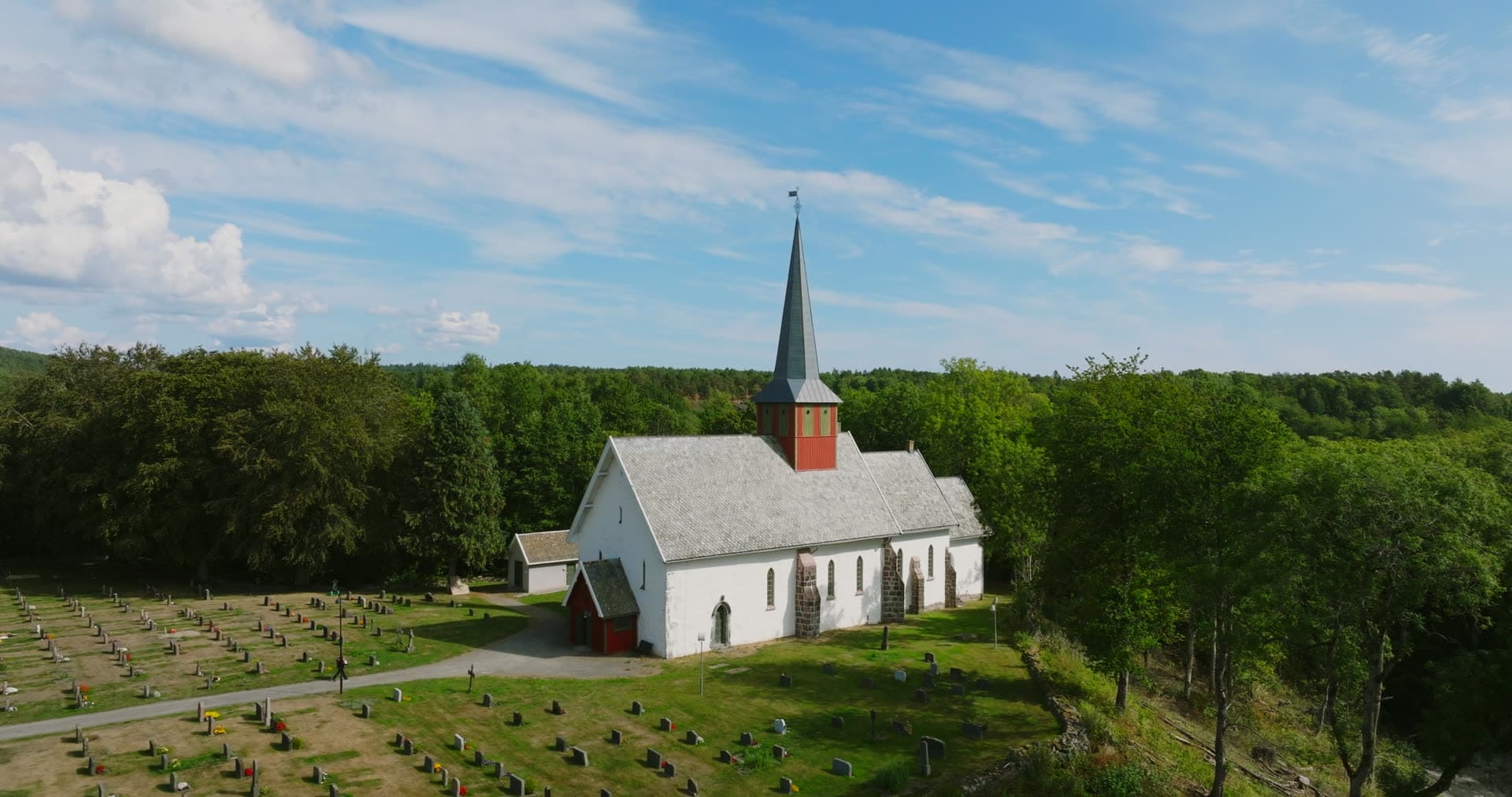 White stone church with red spire and graveyard, Rykene, Norway
