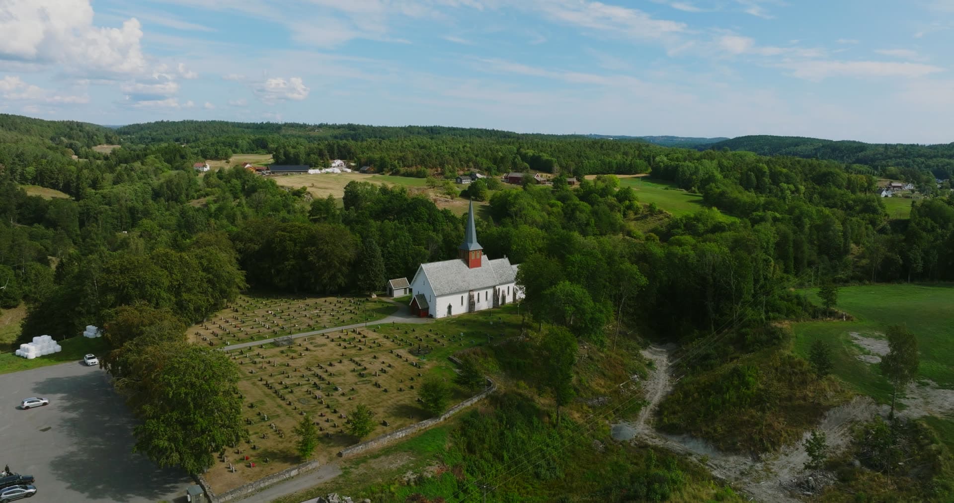 White church and graveyard on wooded hill, Rykene, Norway
