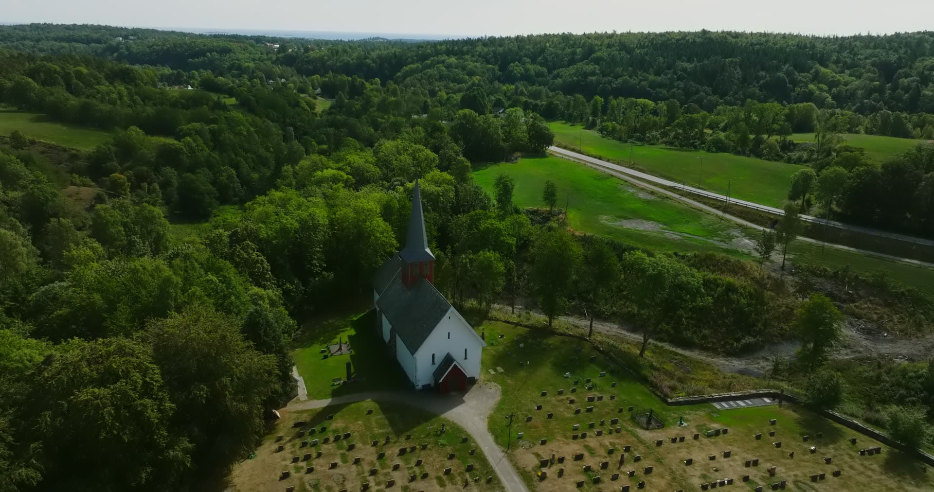 White wooden church and graveyard by woods, Rykene, Norway