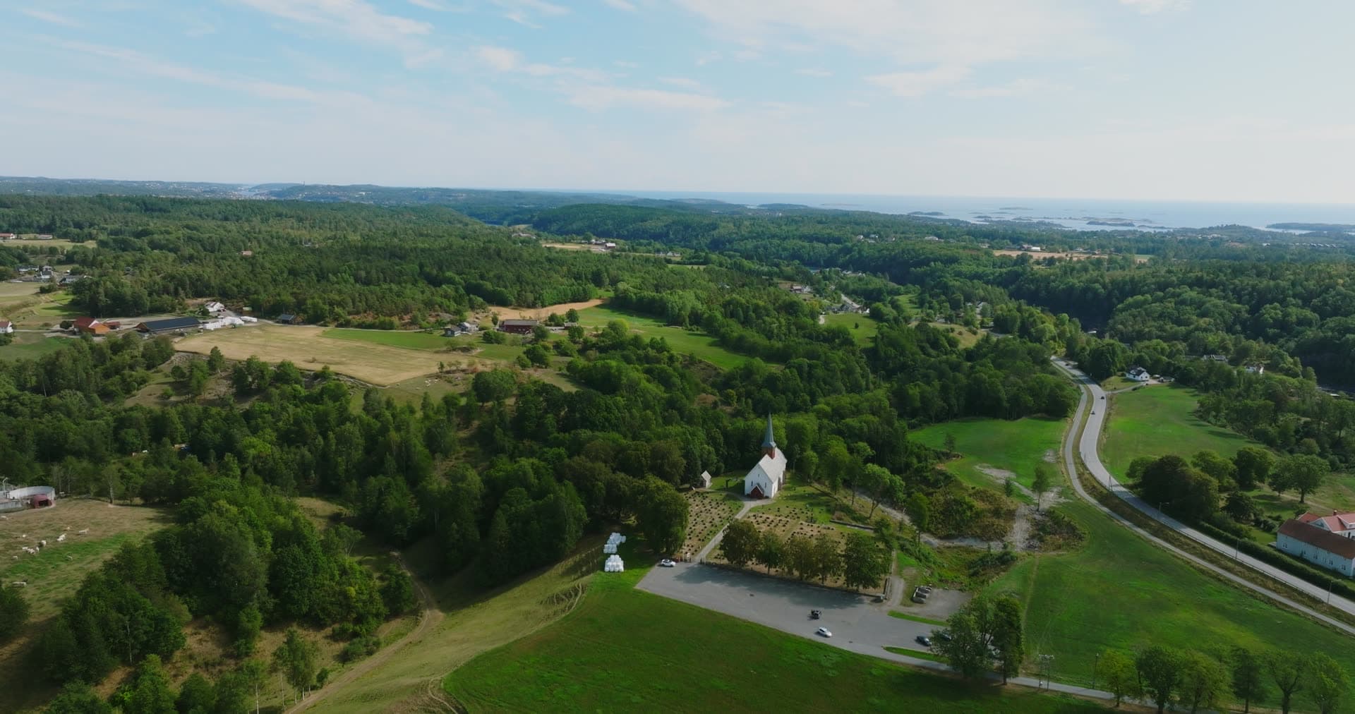 White church and graveyard by farm fields, Rykene, Norway