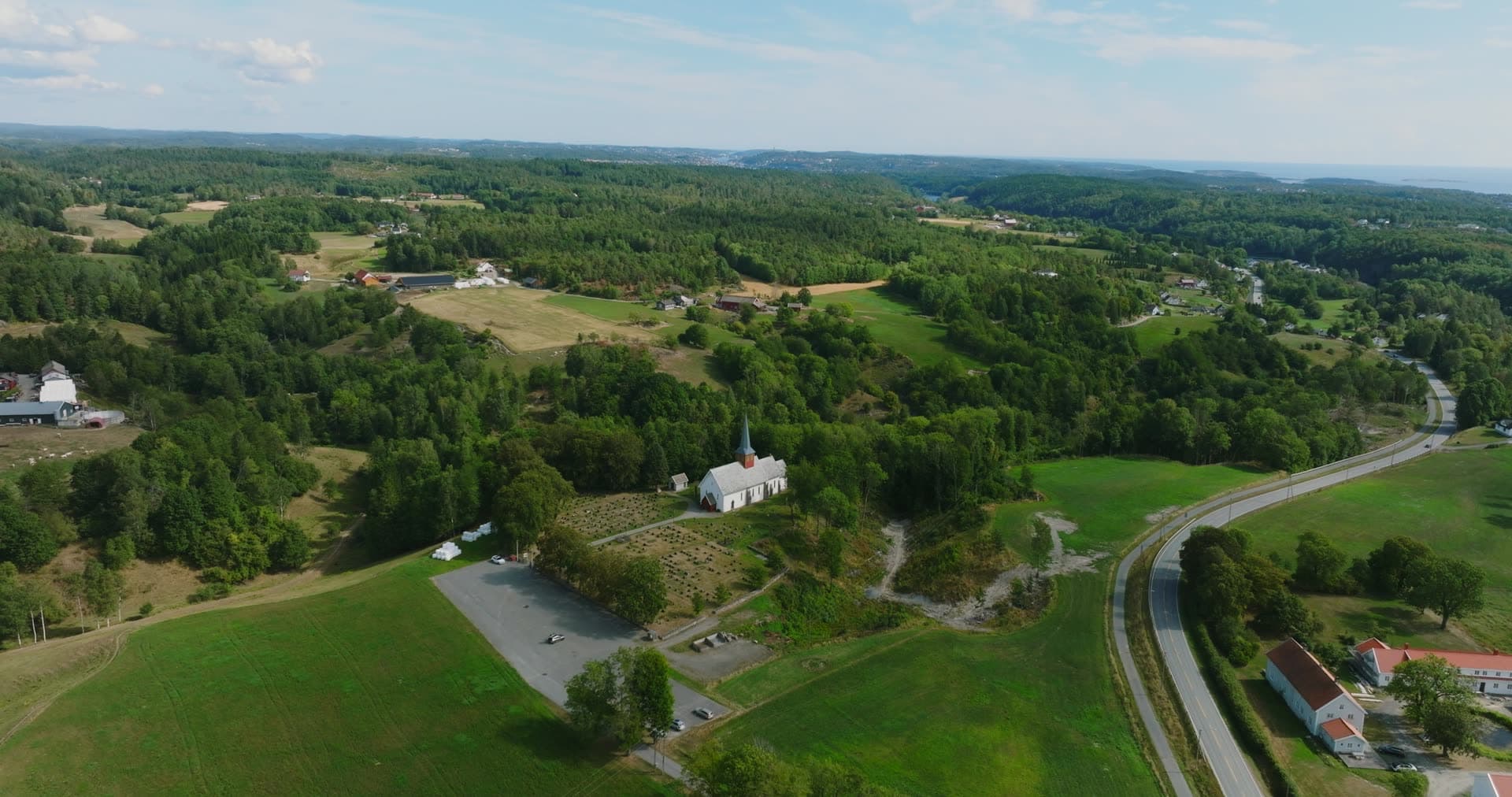 White church and parking lot by farm fields, Rykene, Norway