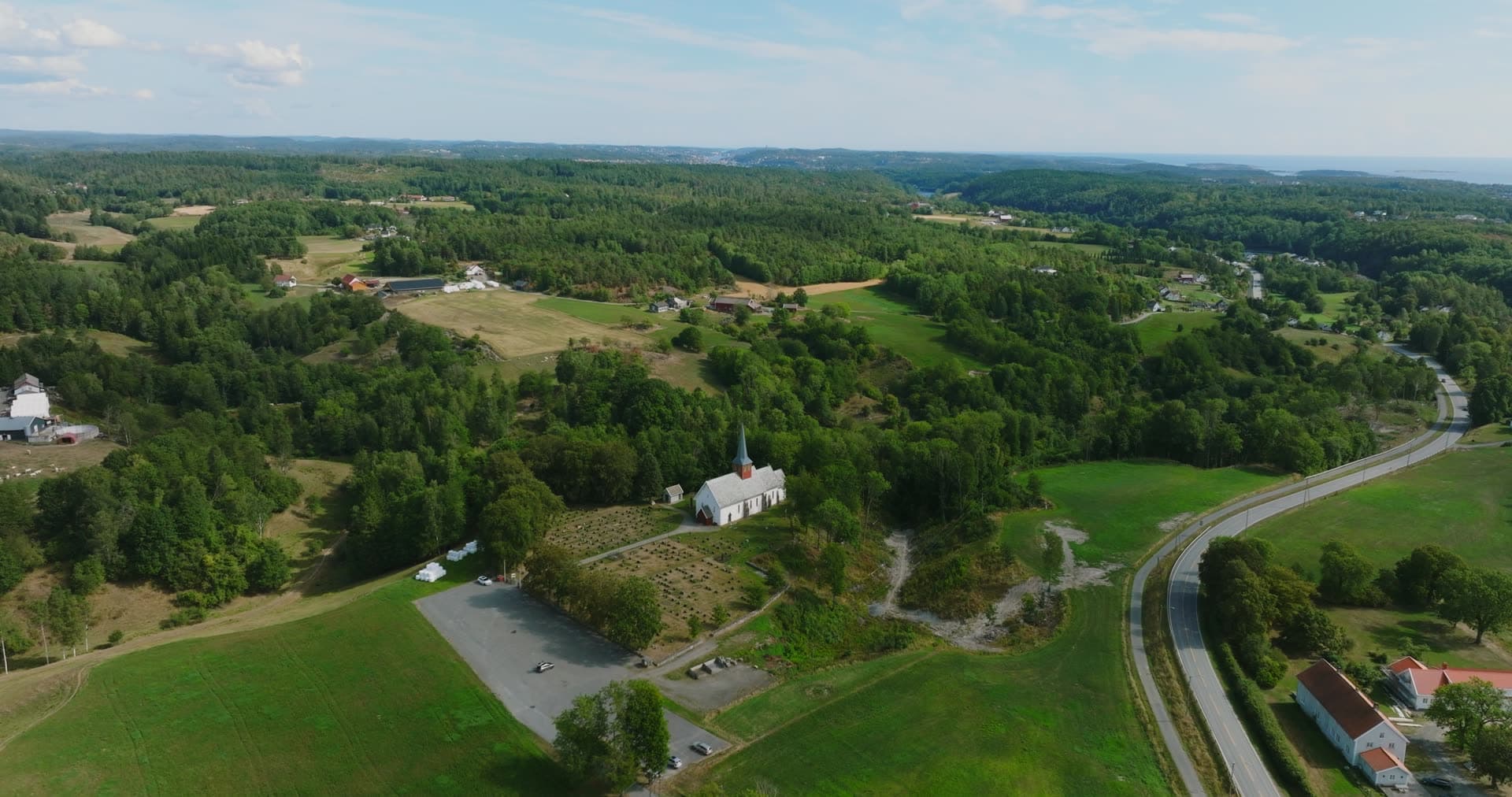 Highway curving past church and parking lot, Rykene, Norway