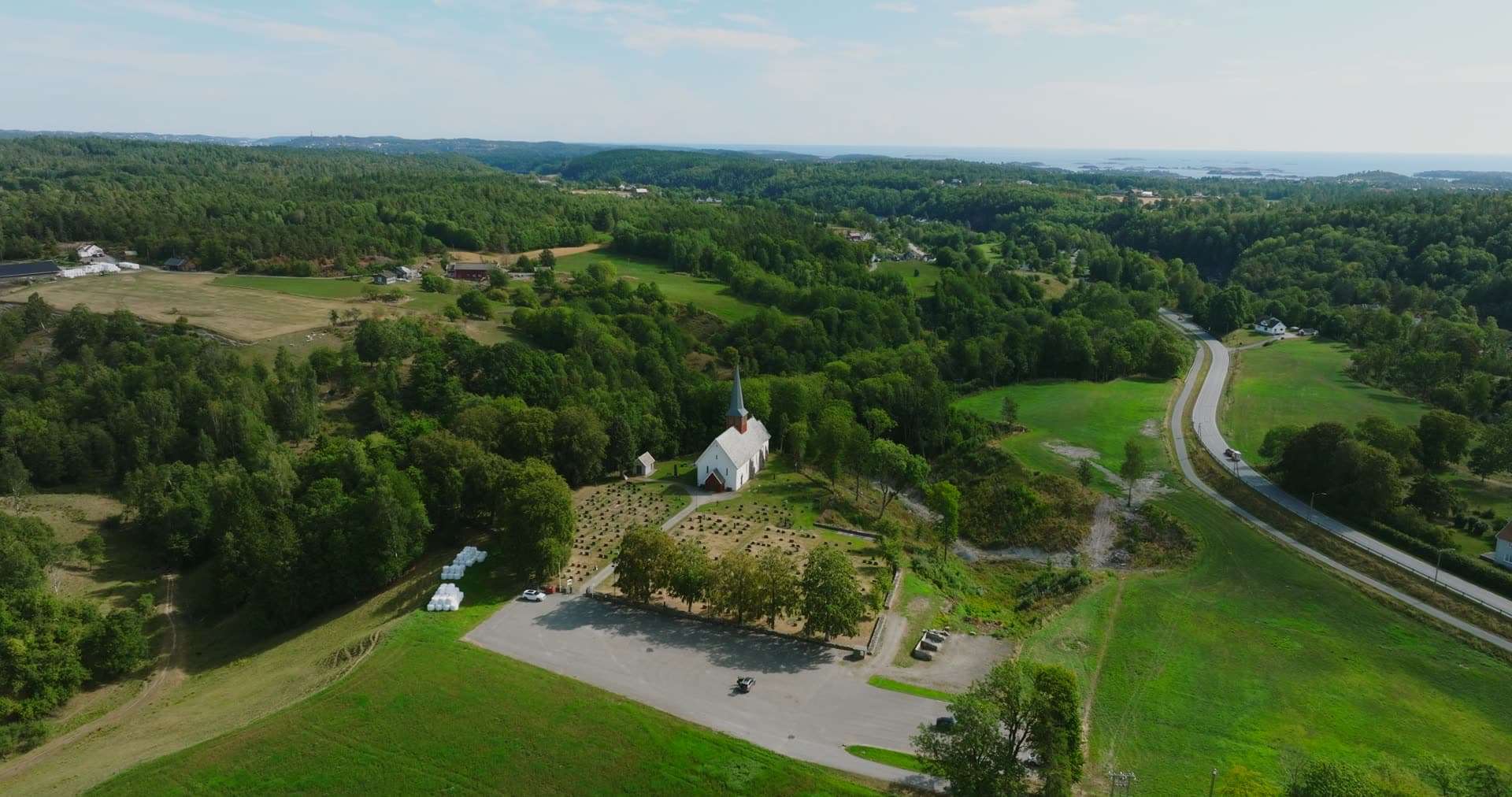 White wooden church and graveyard by highway, Rykene, Norway