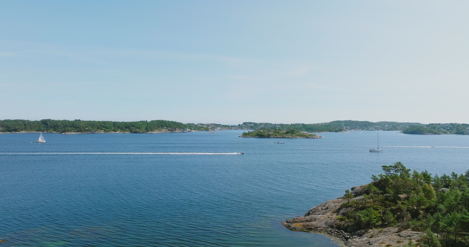 Sailboat and speedboat off a pine-topped point, Skålevik, Norway