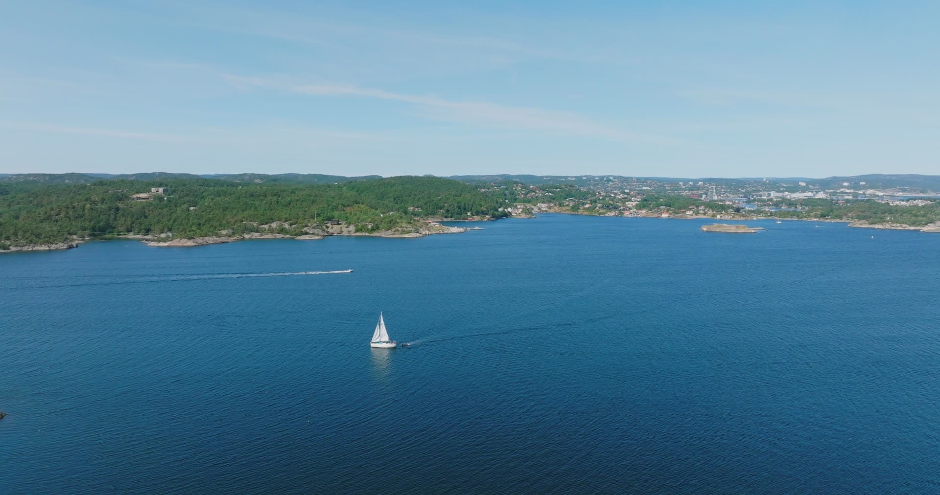 Sailboat off a wooded headland with shore houses, Skålevik, Norway