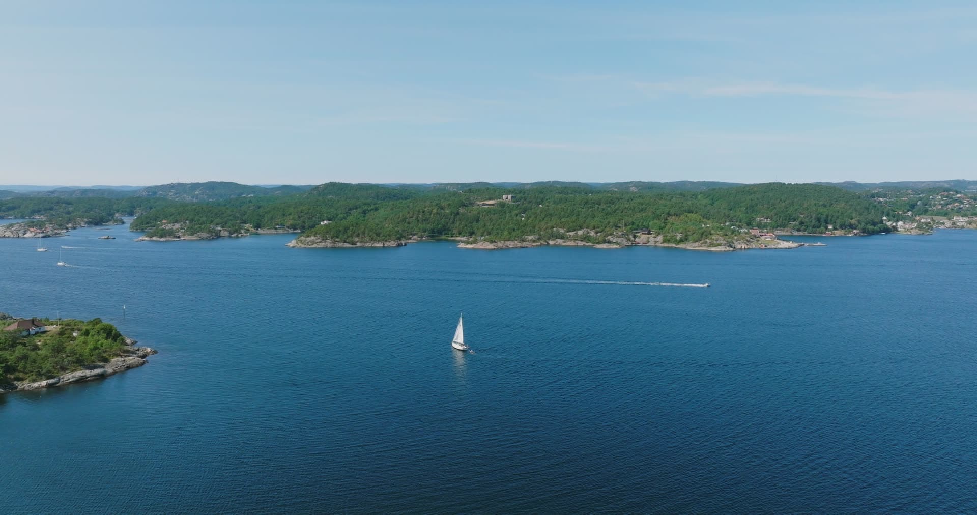 Pine-covered islet and a passing sailboat, Skålevik, Norway
