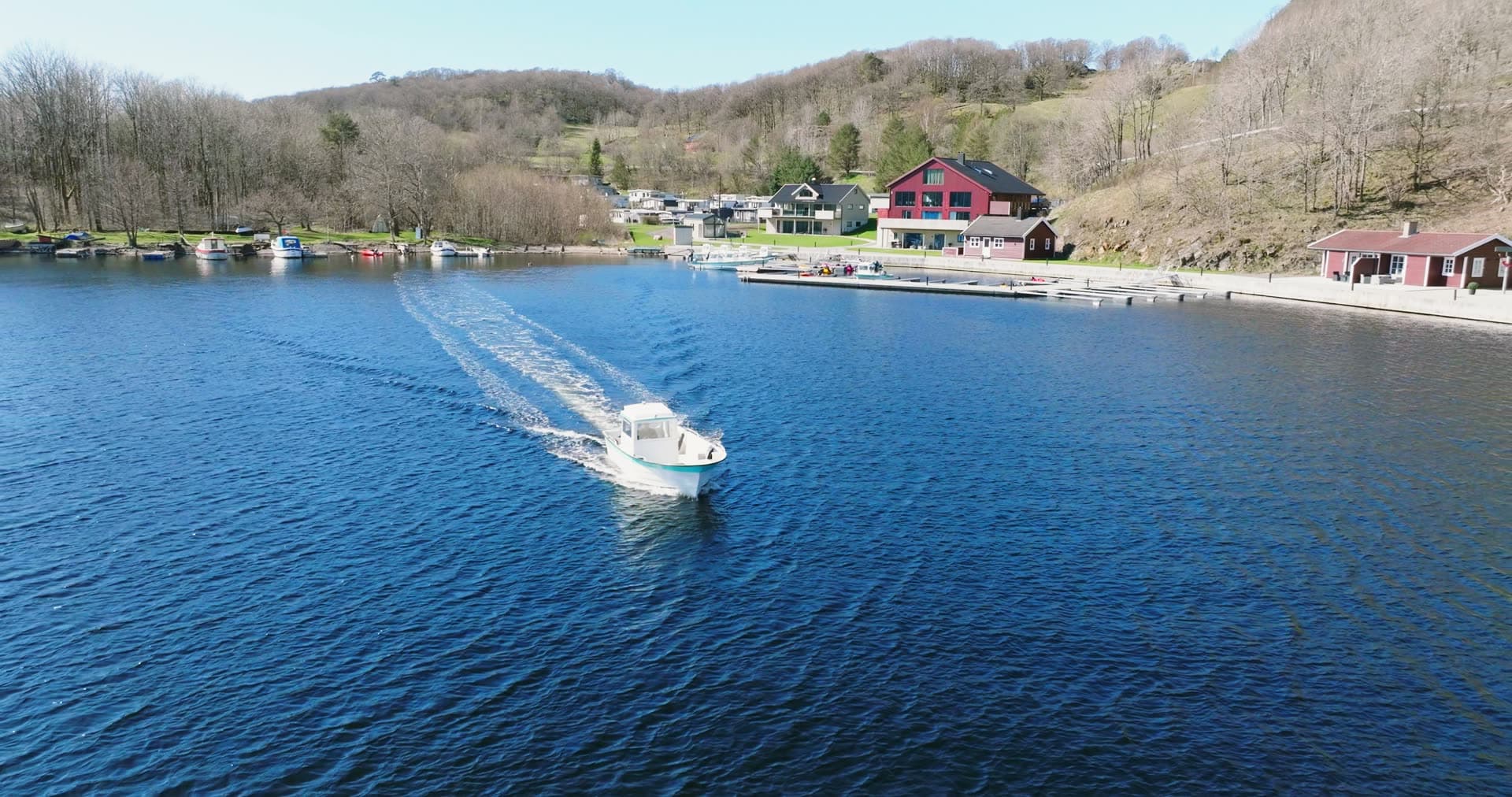 Motorboat wake past red house and docks, Vanse, Norway