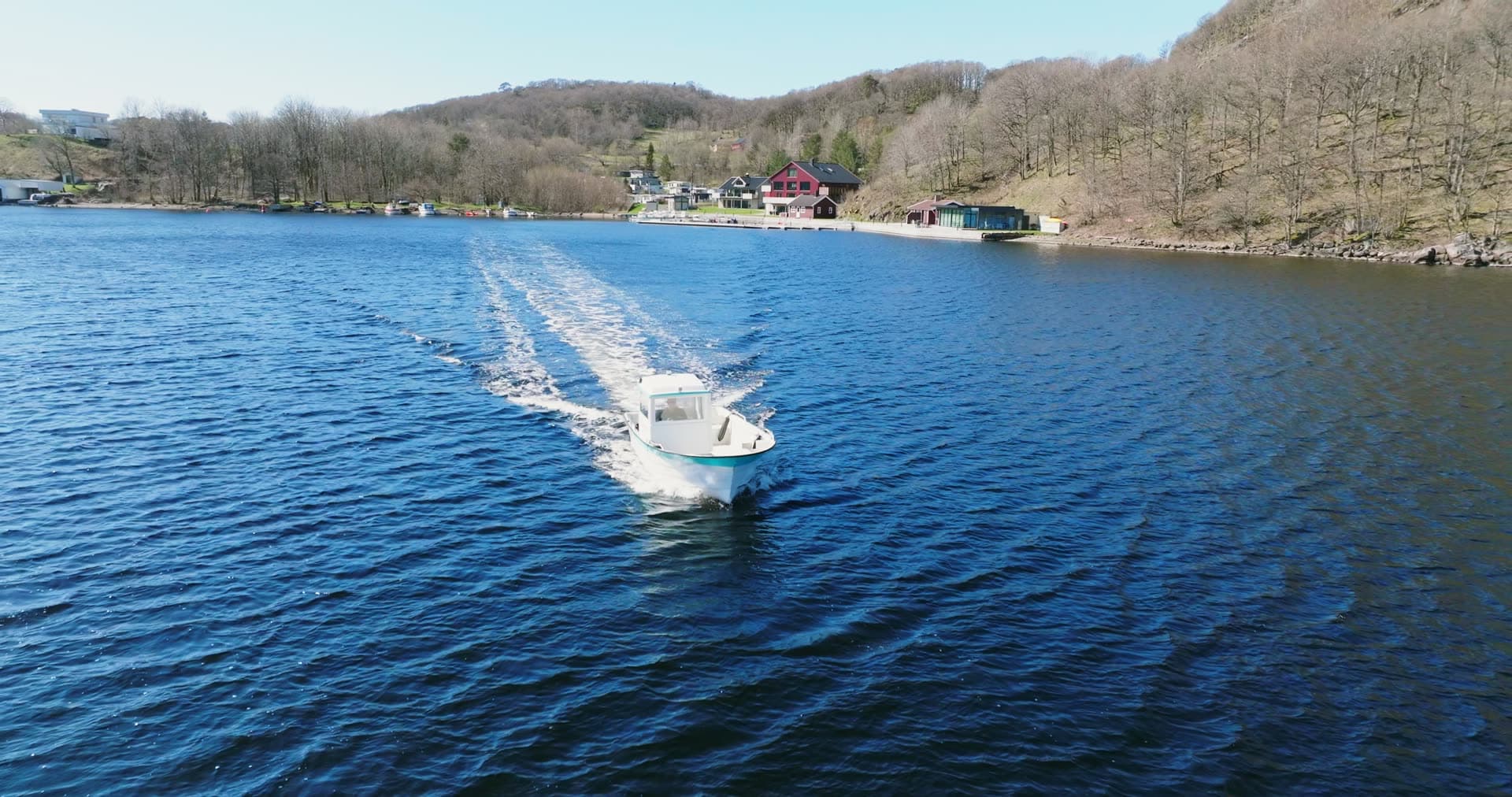 Motorboat trailing wake past red boathouse, Vanse, Norway