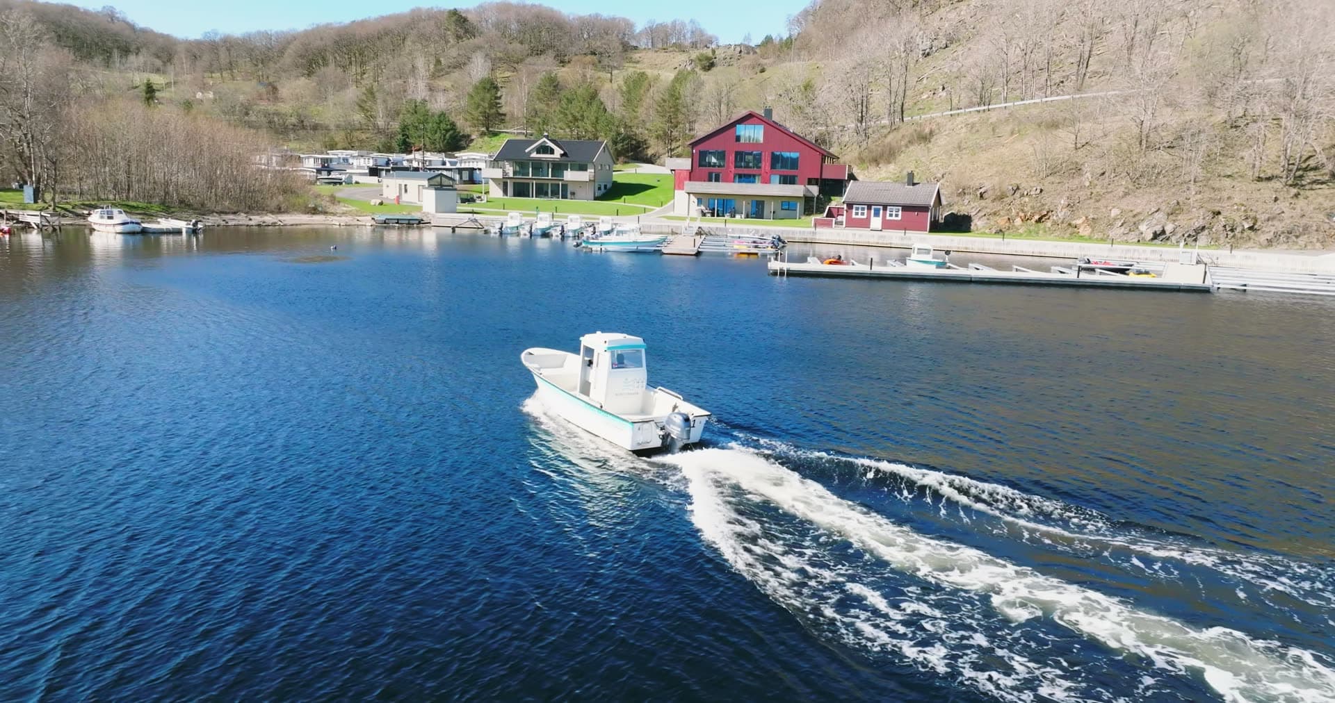 Motorboat leaving docks by red boathouse, Vanse, Norway