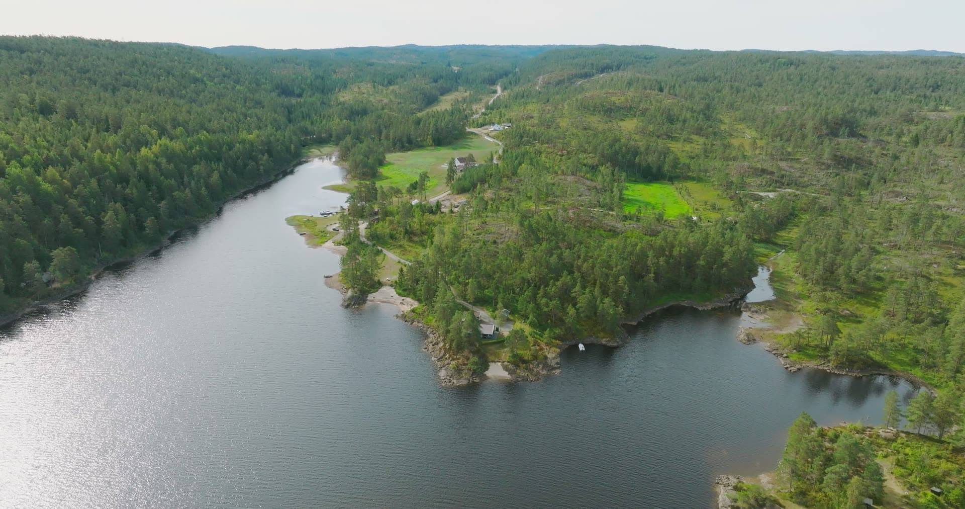 Forested headland and green fields by lake, Vassbotn, Norway