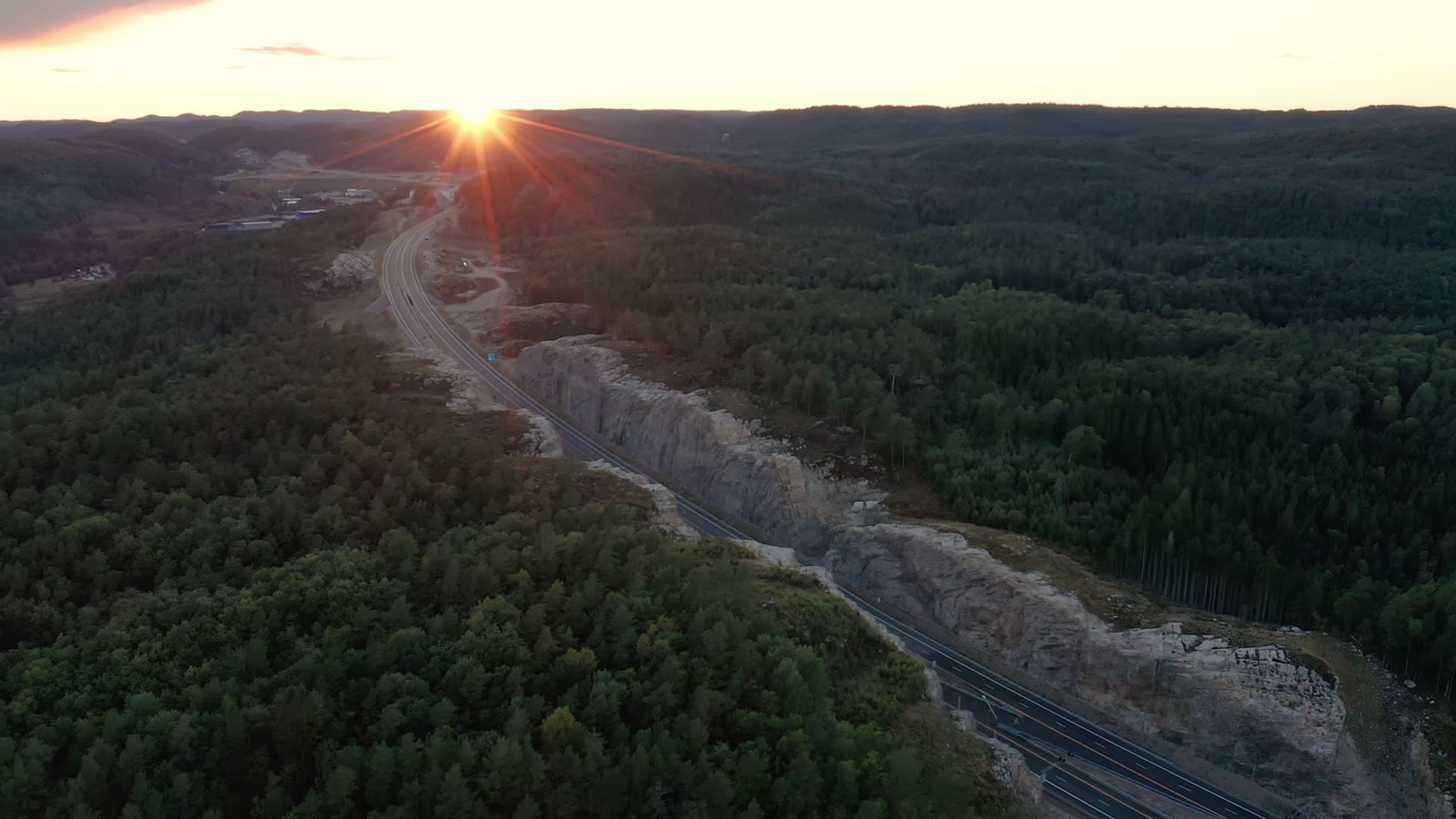 Highway rock cut through forest at sunset, Vedderheia, Norway