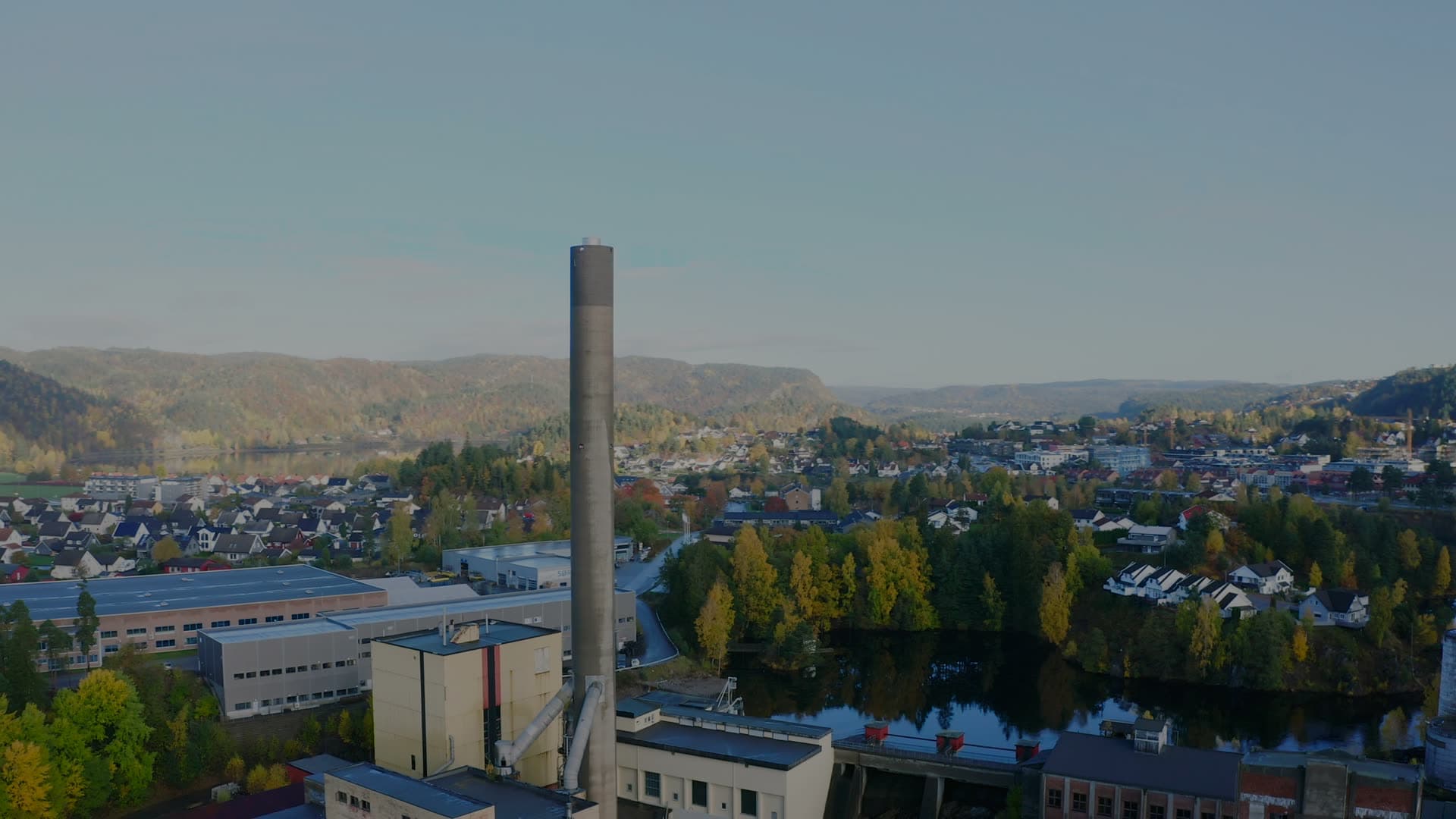 Tall factory chimney beside river town, Vennesla sentrum, Norway