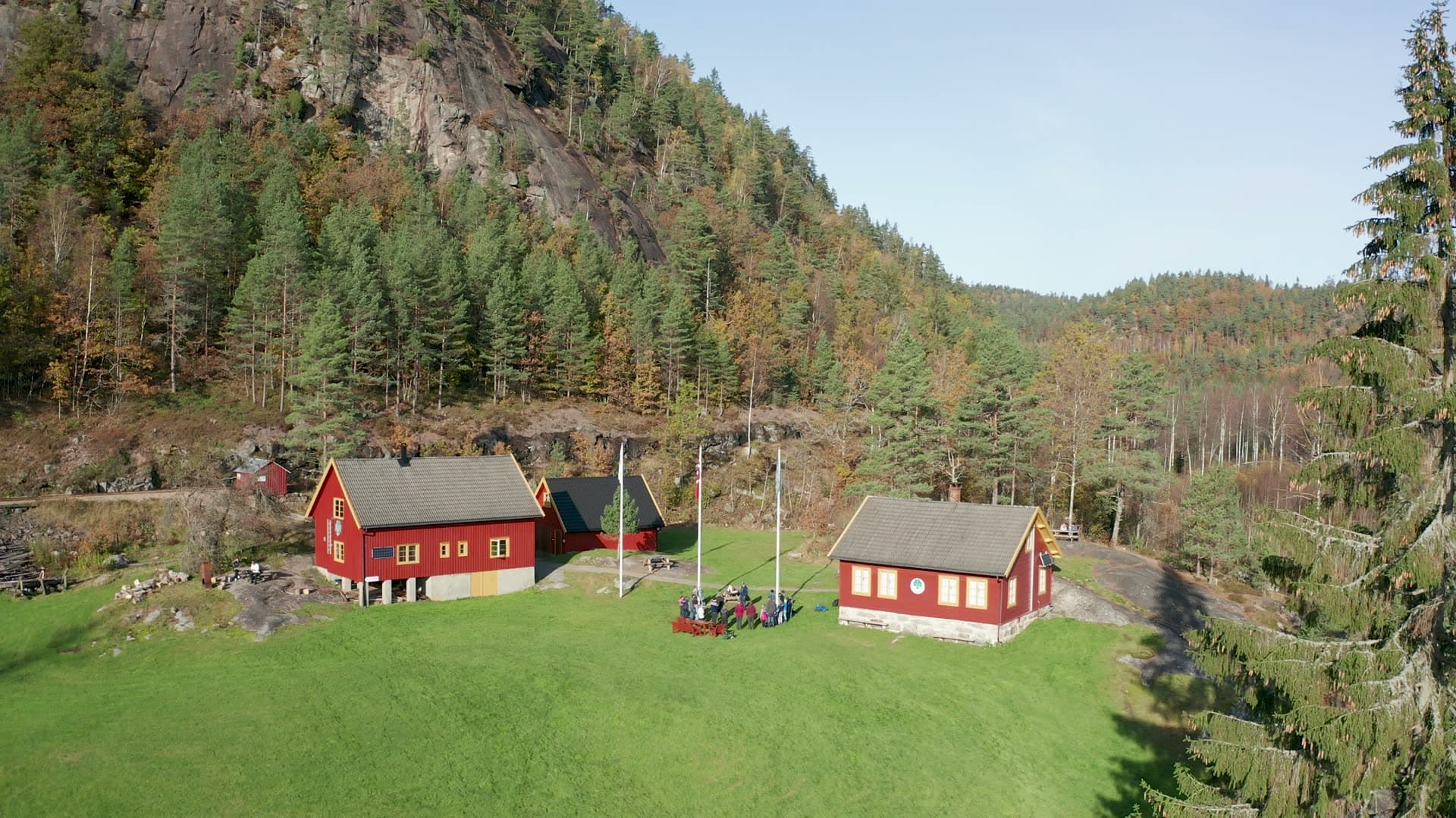 Red farm buildings and flagpoles below cliff, Vennesla, Norway