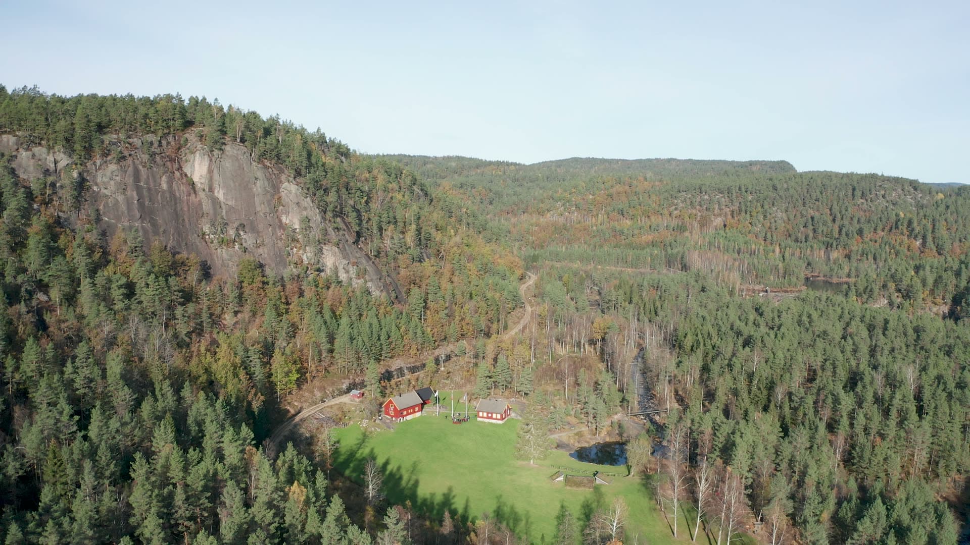 Red farmhouses below bare rock cliff, Vennesla, Norway