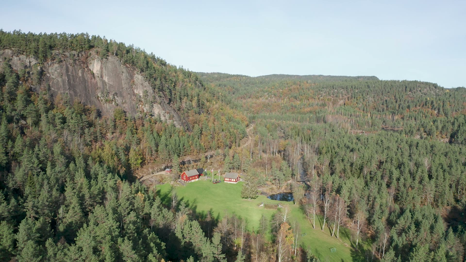 Red farm and pond below a rock cliff, Vennesla, Norway